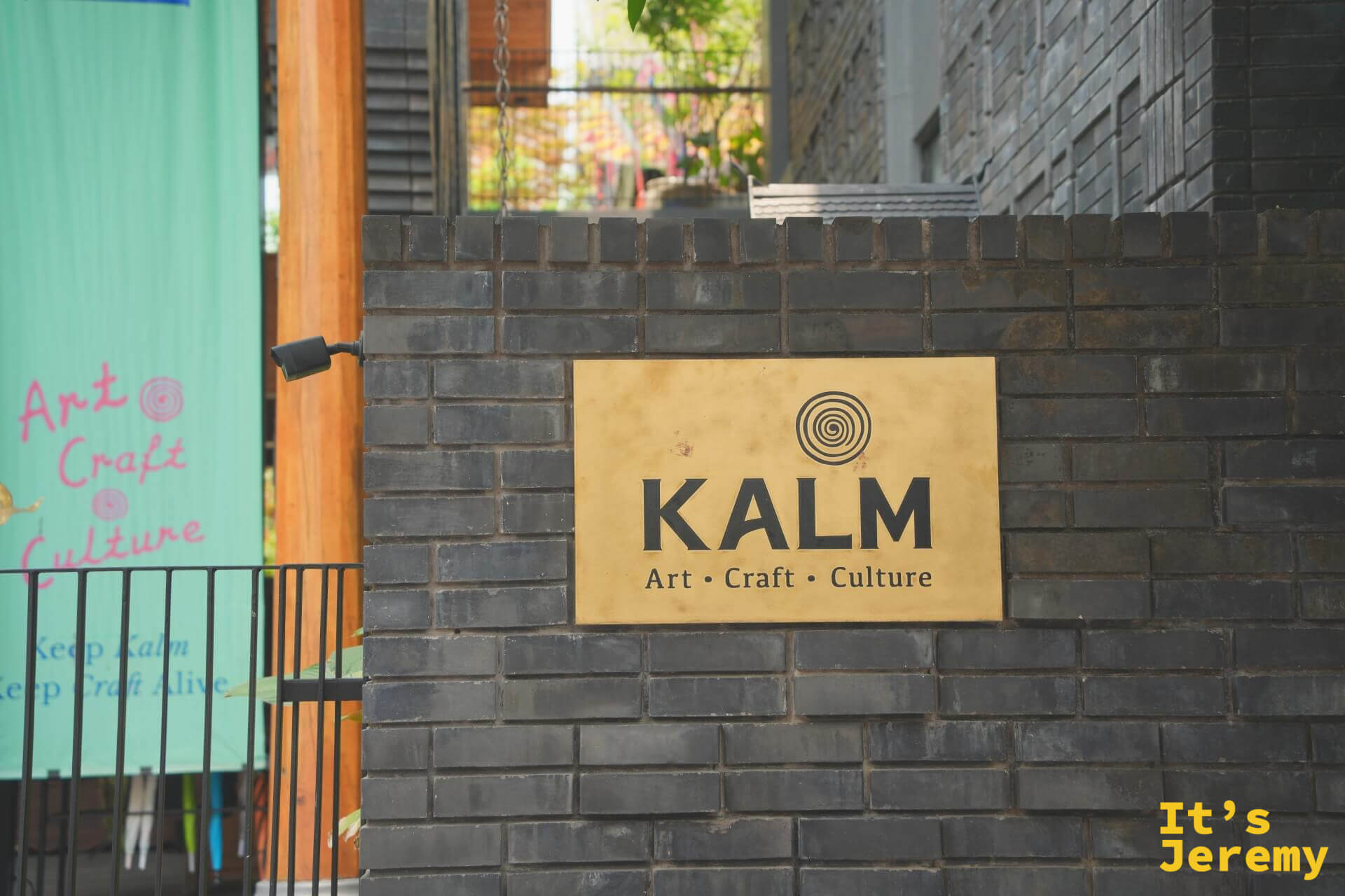 灰磚牆上的金色 KALM 銅牌,寫著 Art・Craft・Culture,左後方是湖水綠的「Keep Kalm, Keep Craft Alive」布旗
