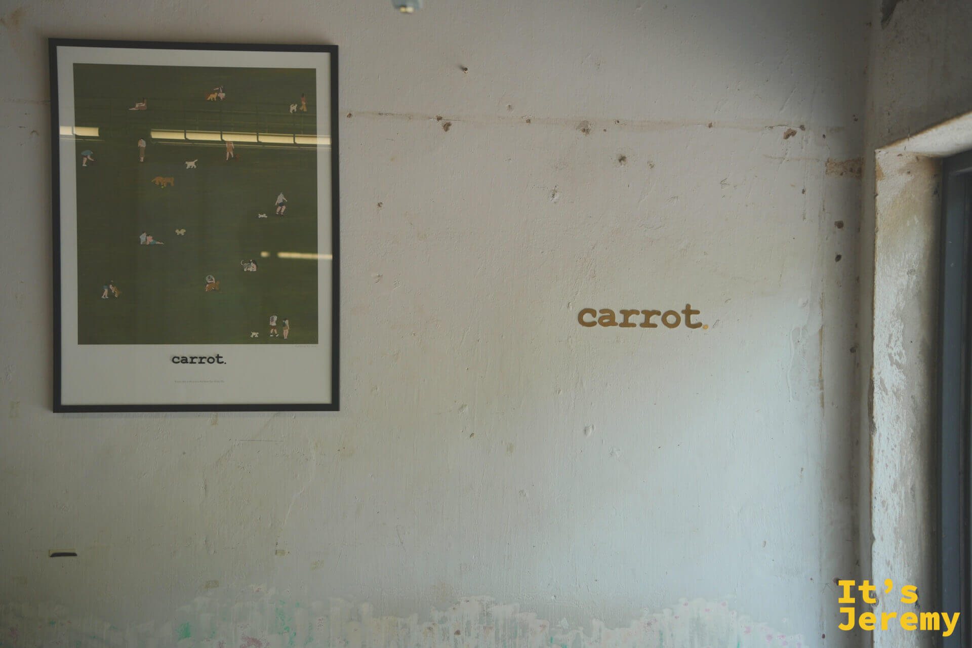白牆上的金色 carrot. 字樣，旁邊掛著一幅以公園草地為主題的插畫海報