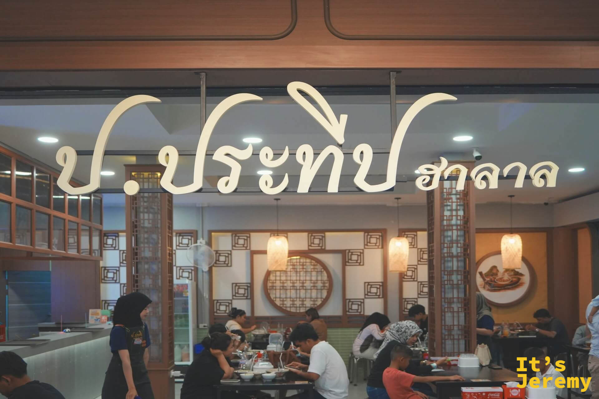 船麵店的米色立體泰文店招掛在挑高門面上，店內木質窗花裝潢，座位坐滿用餐的本地家庭