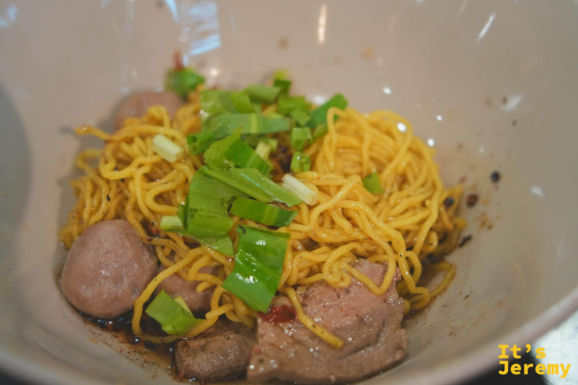 乾拌船麵的特寫，黃色雞蛋麵上鋪著燙牛肉片、牛肉丸與大把翠綠的青菜蔥段