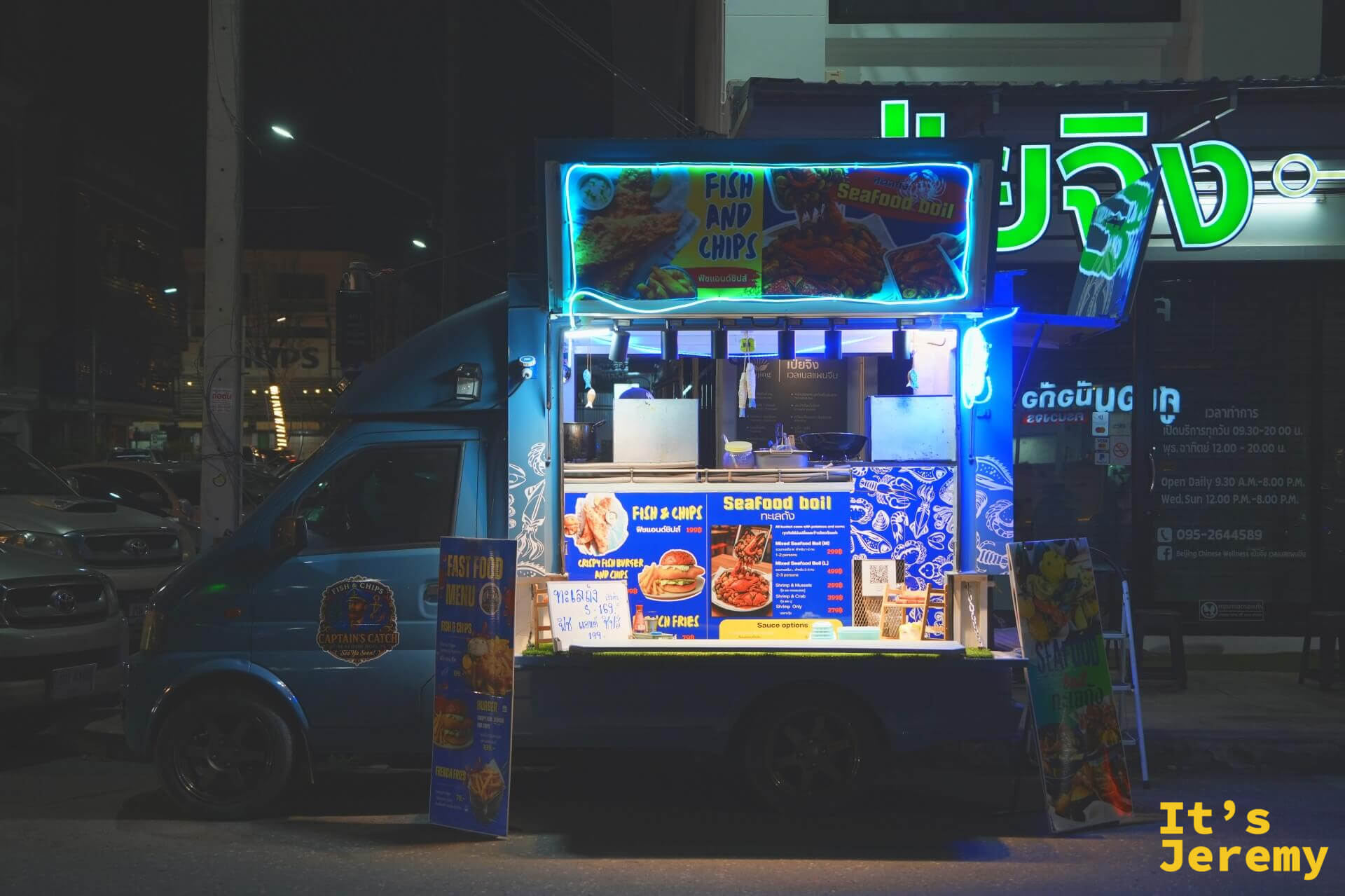 深藍色的炸魚薯條餐車亮著藍色霓虹燈，車身掛著 Fish and Chips 與 Seafood Boil 的菜單看板