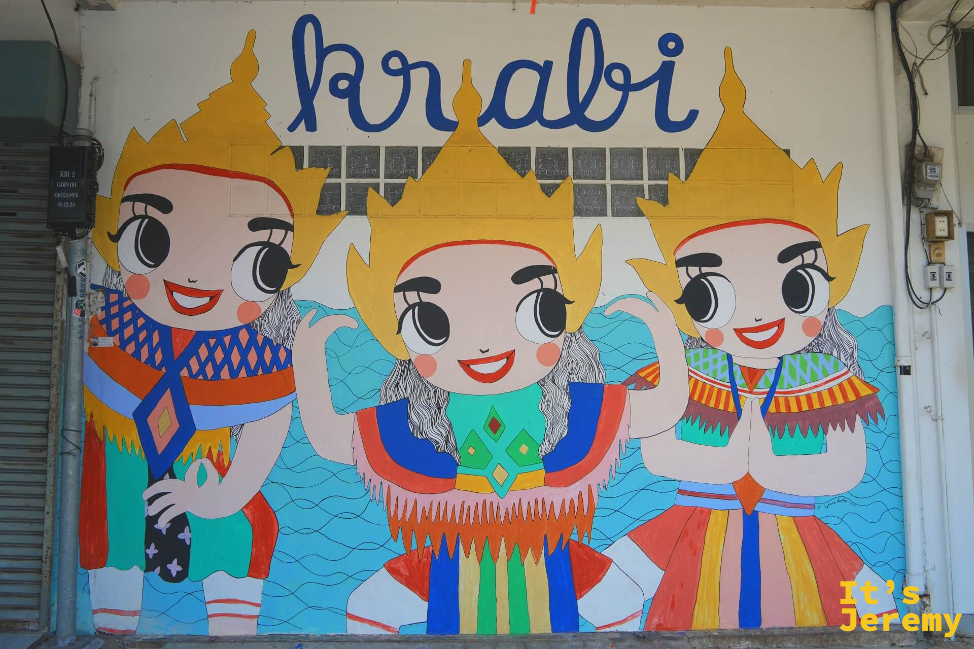 喀比鎮街邊的 Krabi 彩繪壁畫,三個卡通泰式舞者在藍色浪紋背景前,上方寫著「Krabi」藍色手寫字