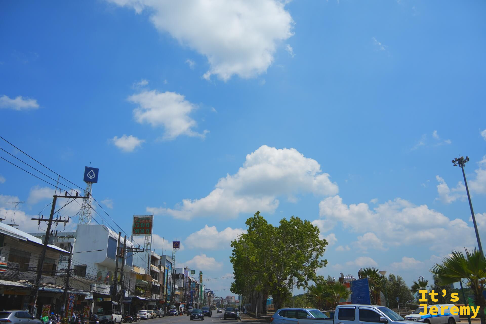 喀比鎮市區主幹道,藍天白雲、兩側商店招牌排開,一棵大樹矗立路中央