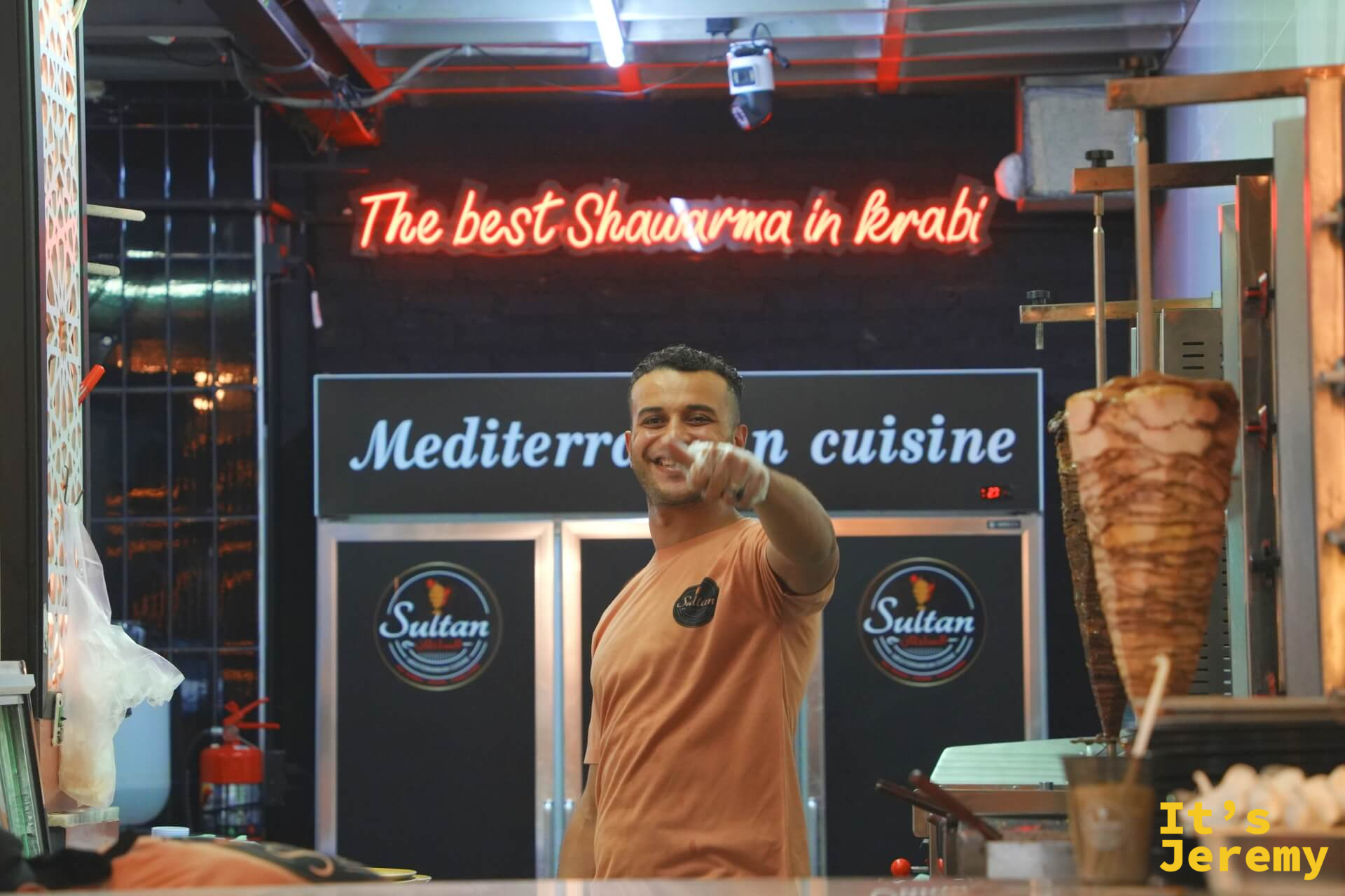 Sultan 攤位，老闆在「The best Shawarma in Krabi」霓虹燈前比讚