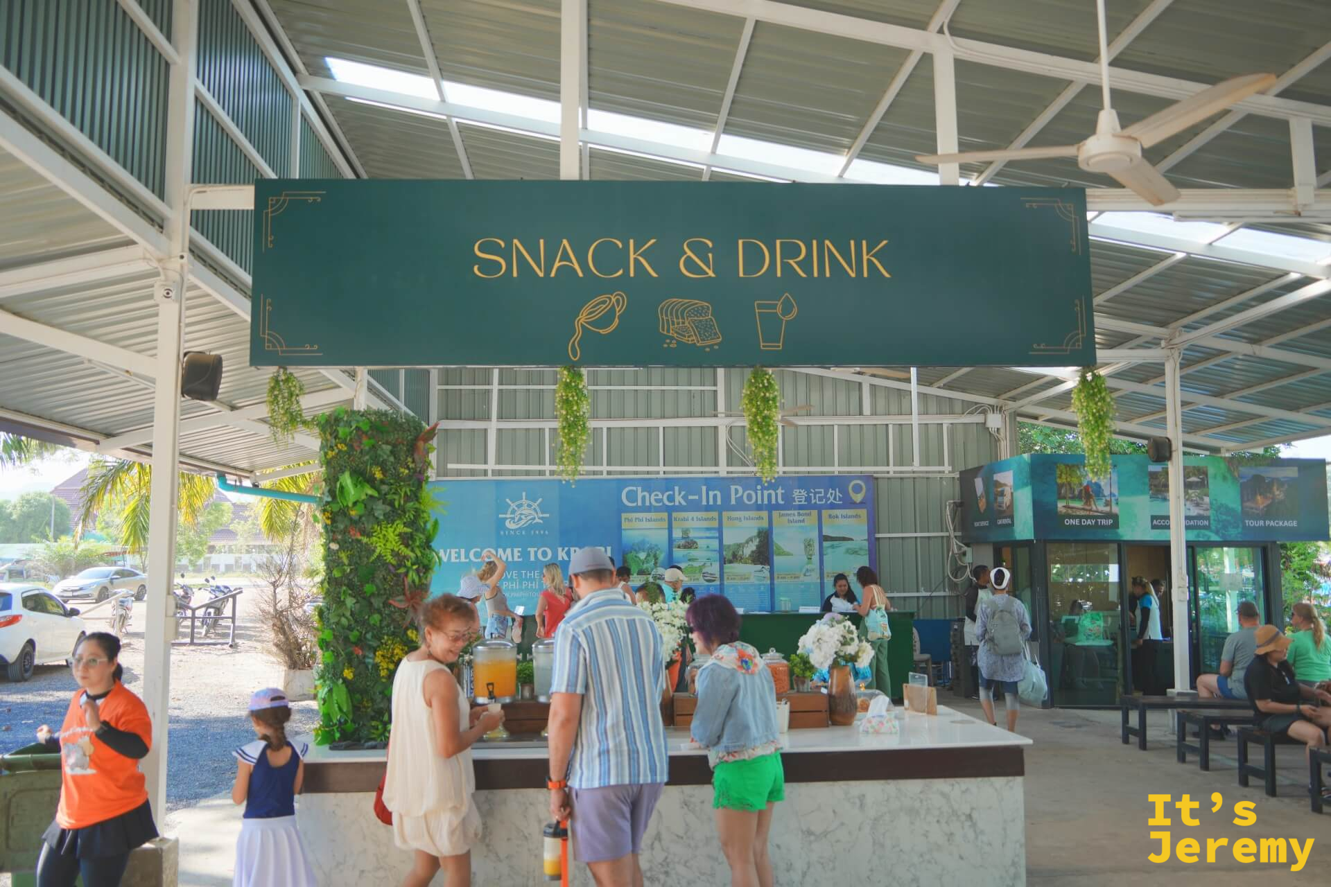 報到處的 Snack & Drink 吧台，旅客在取用飲料，後方有 Check-In Point 登記處