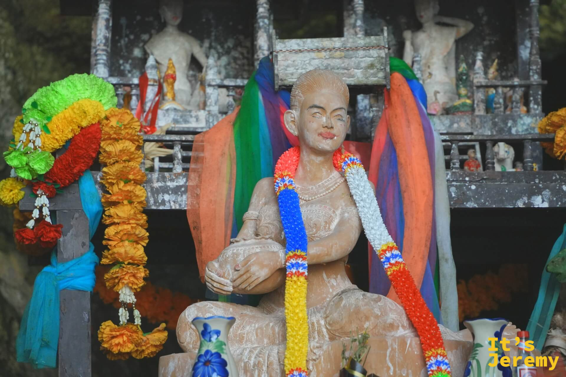 帕南女神像特寫——面容平靜,頸上掛著多彩花環,神龕後方還有其他小像