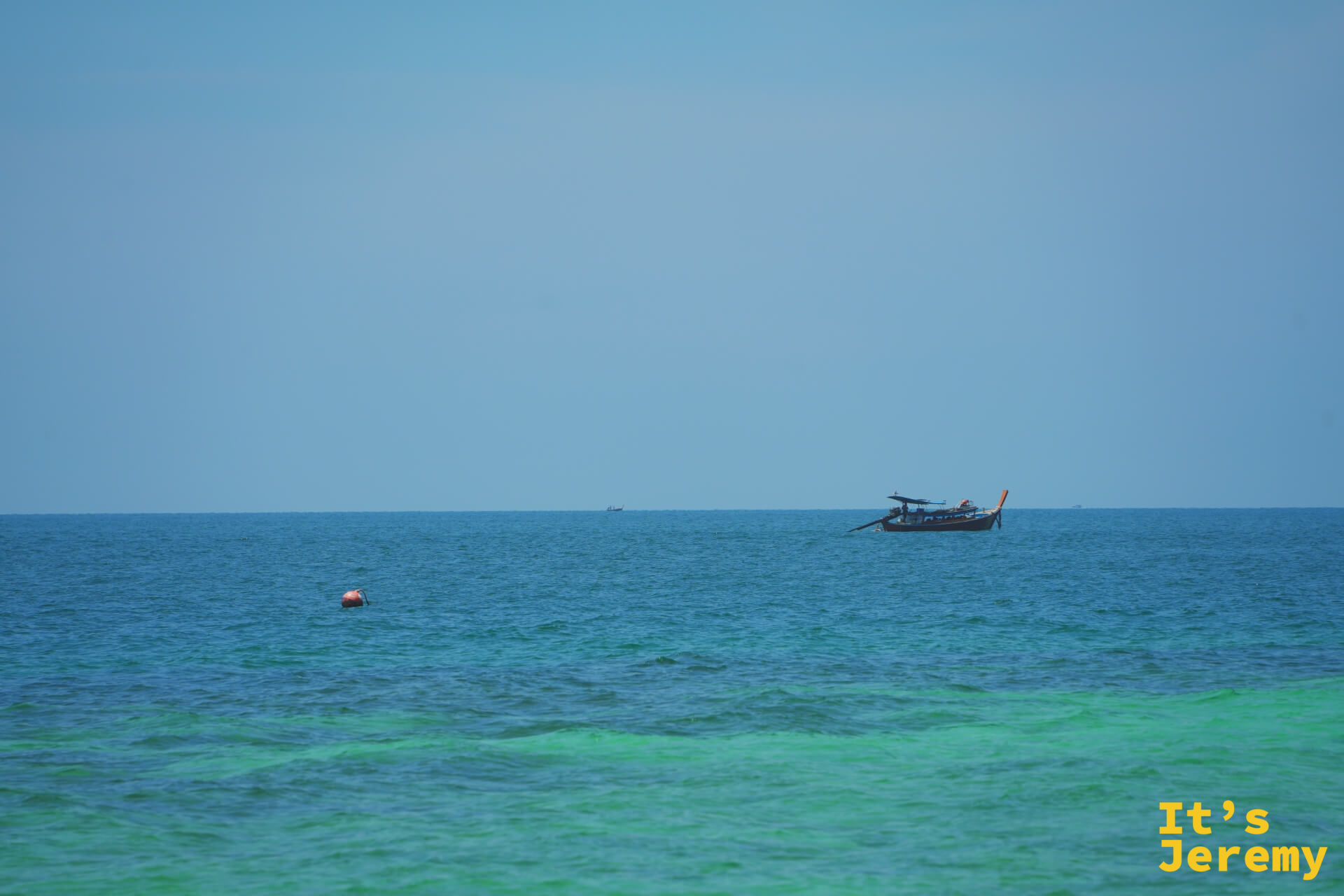 水平線上,長尾船在藍綠色海面上緩行,海天色彩層次分明