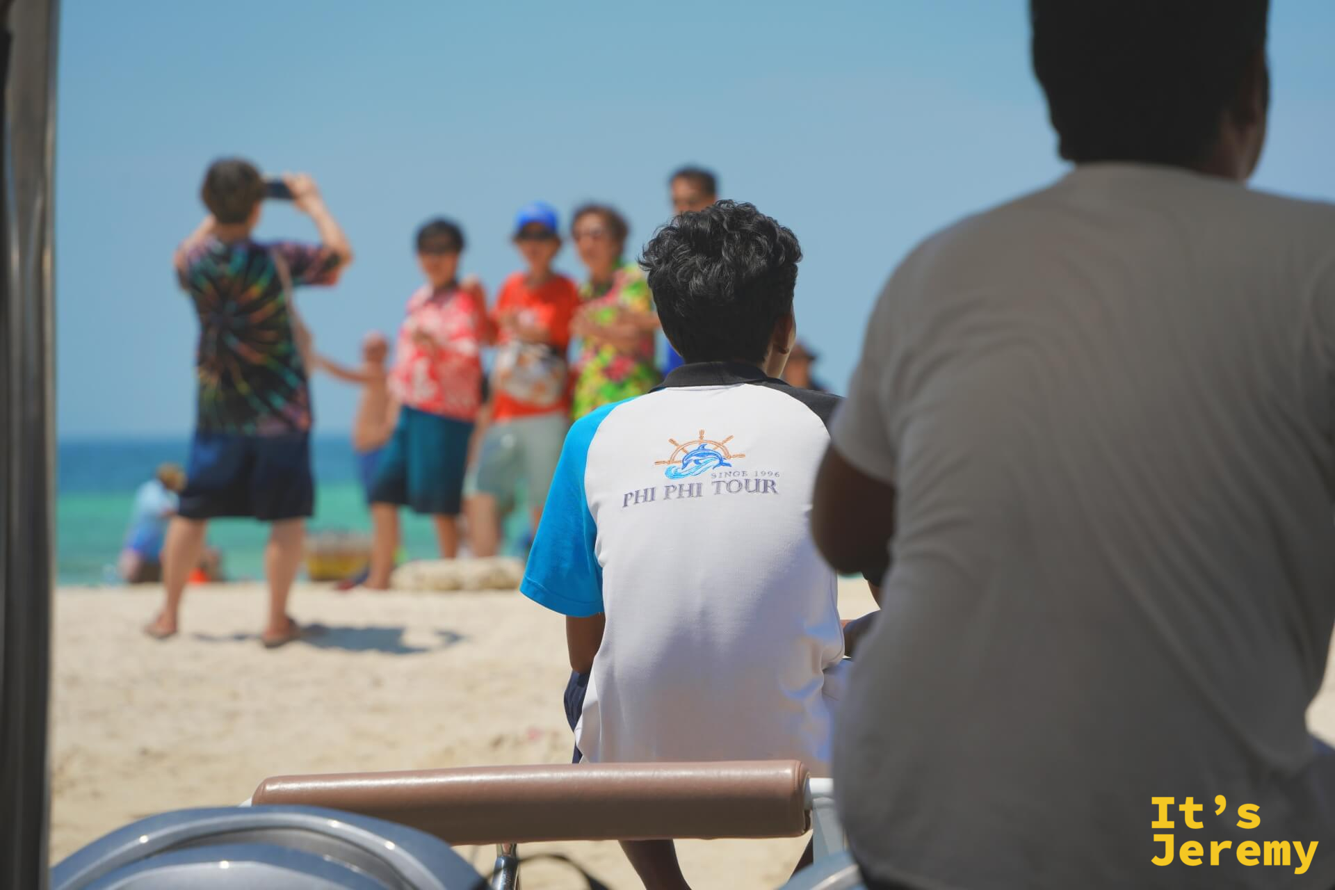 從船艙往外看,PHI PHI TOUR 導遊背對鏡頭,前方沙灘上旅客正在拍照