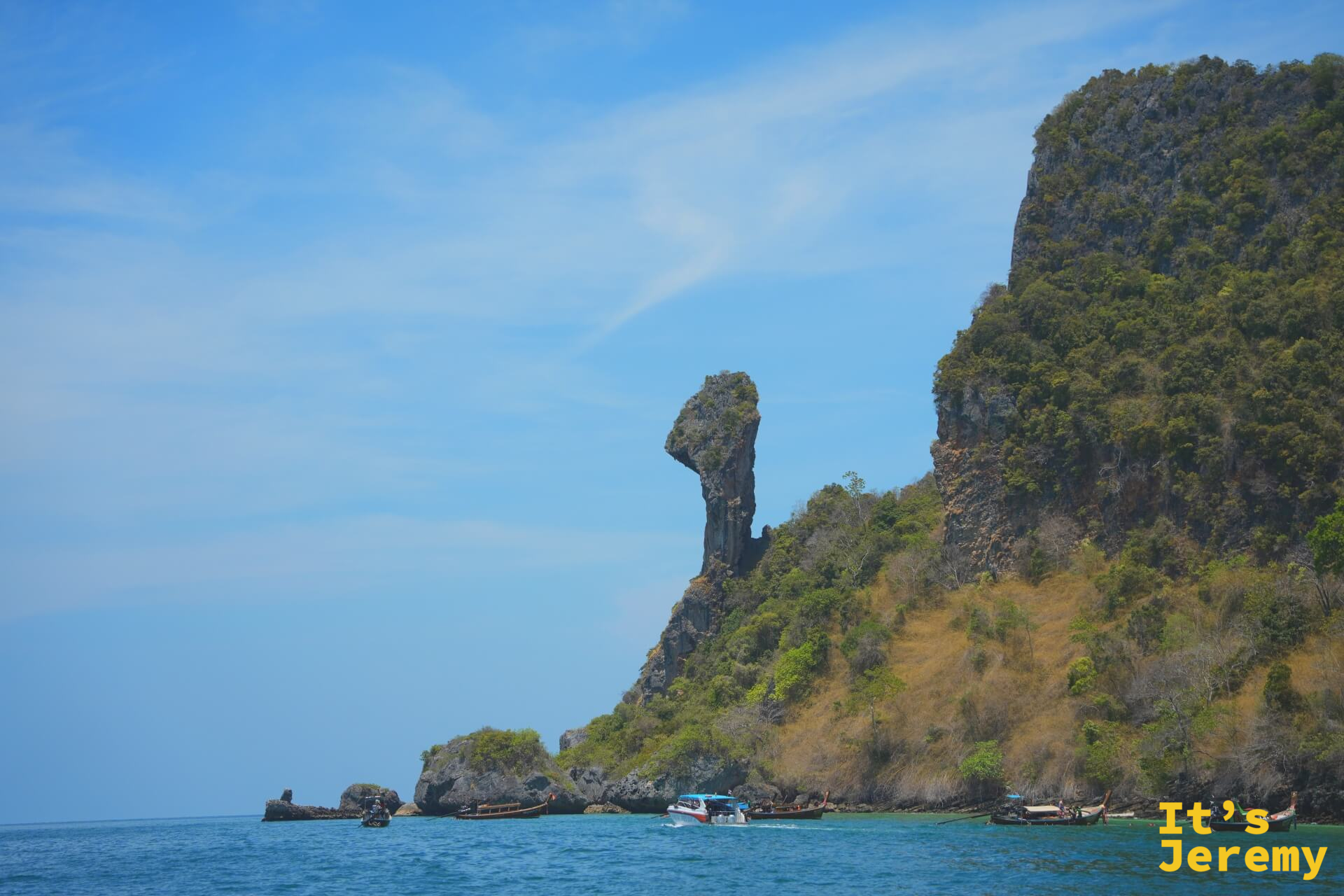 從海面遠眺雞頭岩，石灰岩柱從懸崖邊緣斜伸而出，輪廓像一隻昂首的公雞