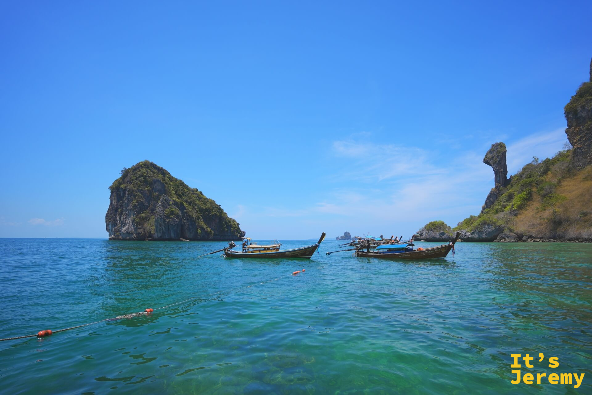 多艘長尾船在 Koh Si 旁的翡翠海面上並排停靠，遠處另一座石灰岩小島清晰可見