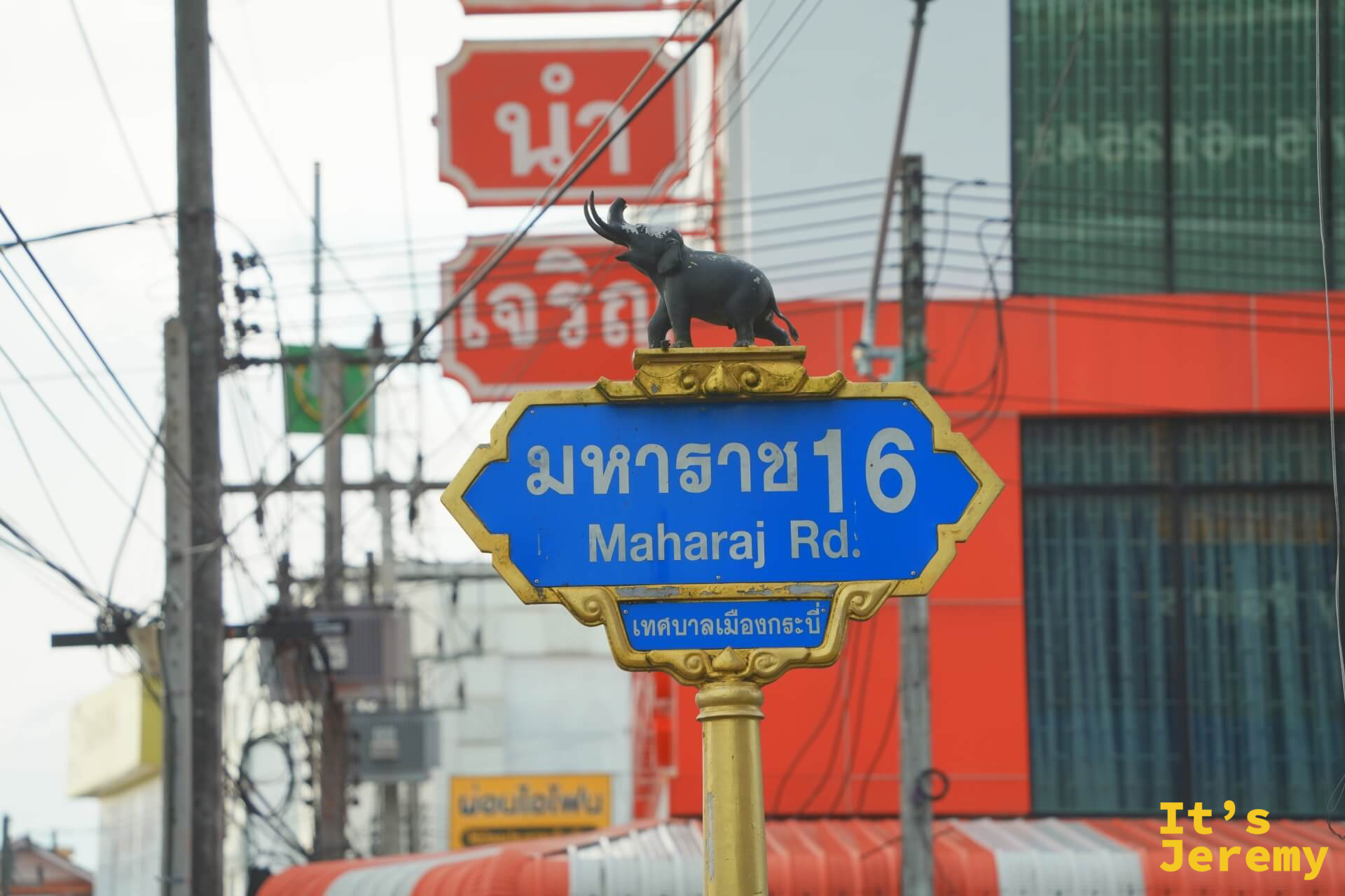 Maharaj Road 金框路牌特寫，頂端有象雕塑，背景是傍晚的市區街道