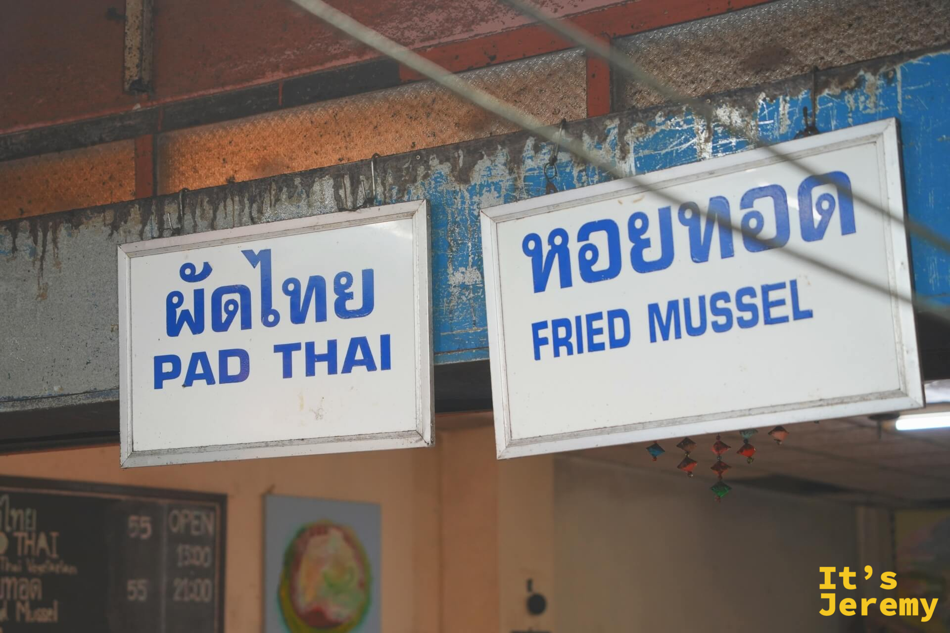 掛牌招牌上寫著 PAD THAI 與 FRIED MUSSEL，藍底白字，掛在老攤棚架上