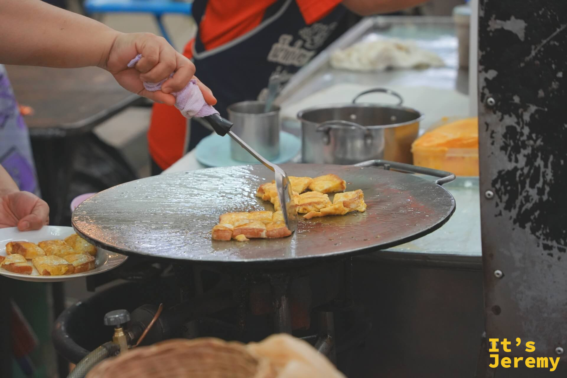 師傅在大圓鐵板上用鏟子翻動沾了蛋液的麵包片，旁邊已有一盤完成品在等候。