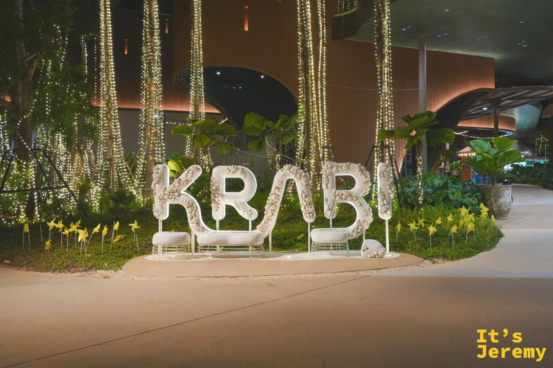 白色珊瑚貝殼造型的 KRABI 大字裝置,背後有燈光瀑布樹與綠色植栽