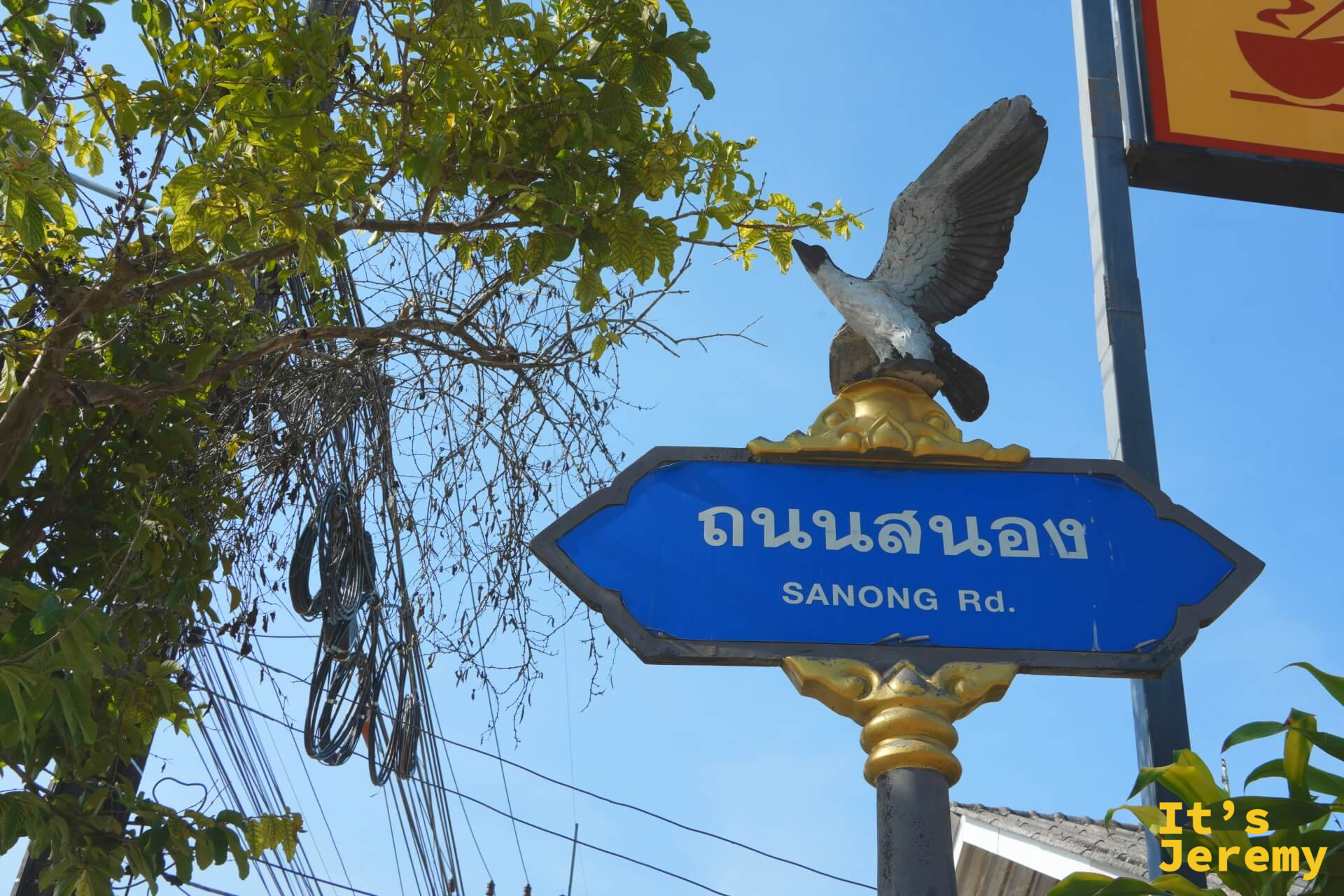 喀比市區 Sanong Rd. 路牌,藍色路牌頂端是一隻展翅的鷹形雕塑