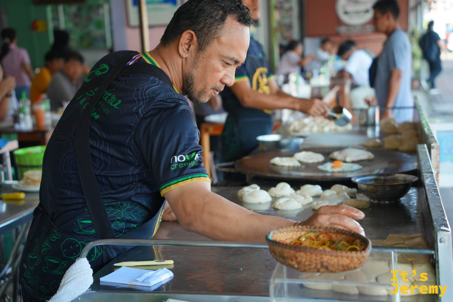 師傅雙手整理麵糰球，鐵板上同時煎著多張 Roti