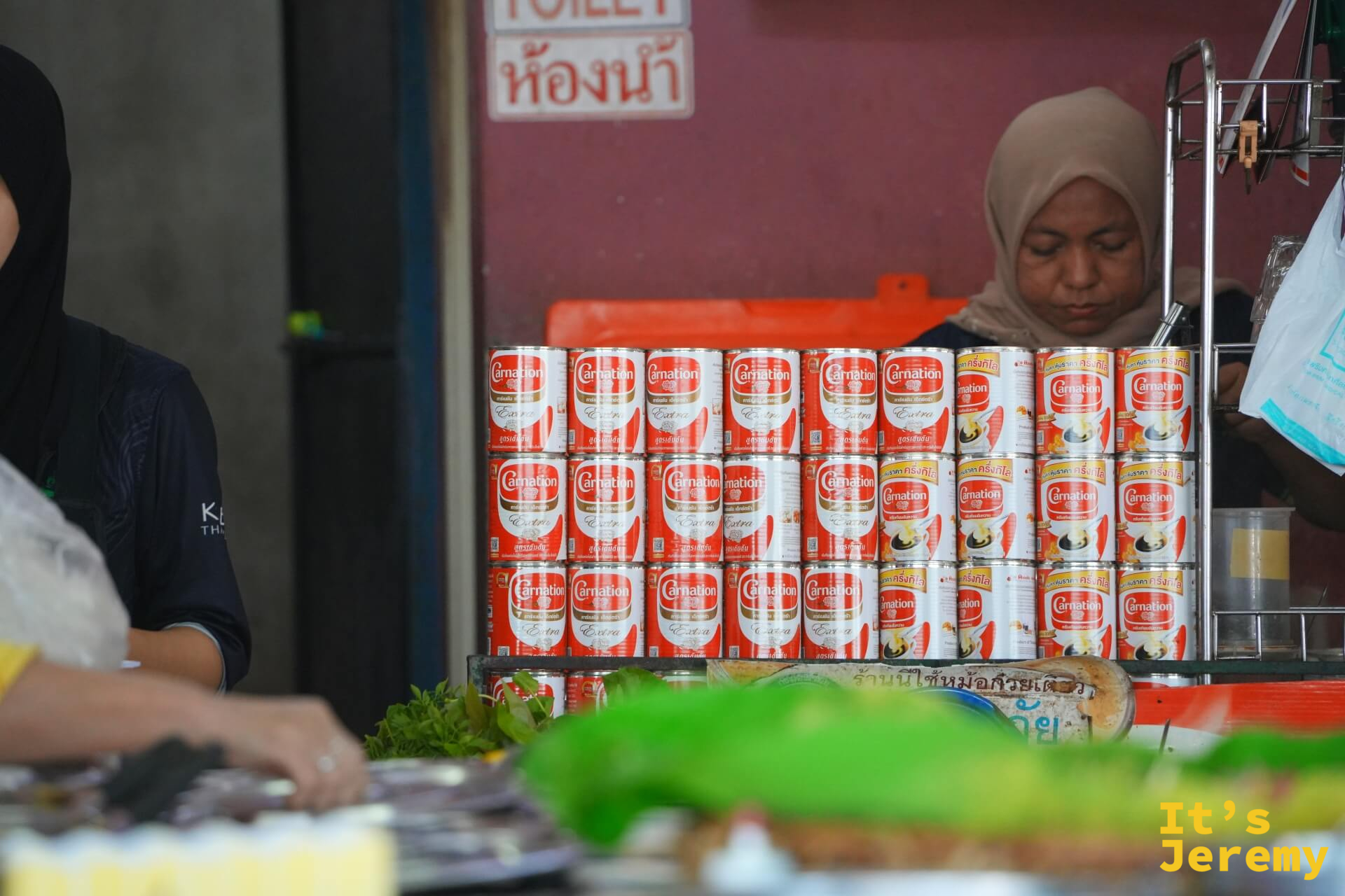 Carnation 煉乳罐整齊堆疊在吧檯旁，是 Teh Tarik 的核心原料