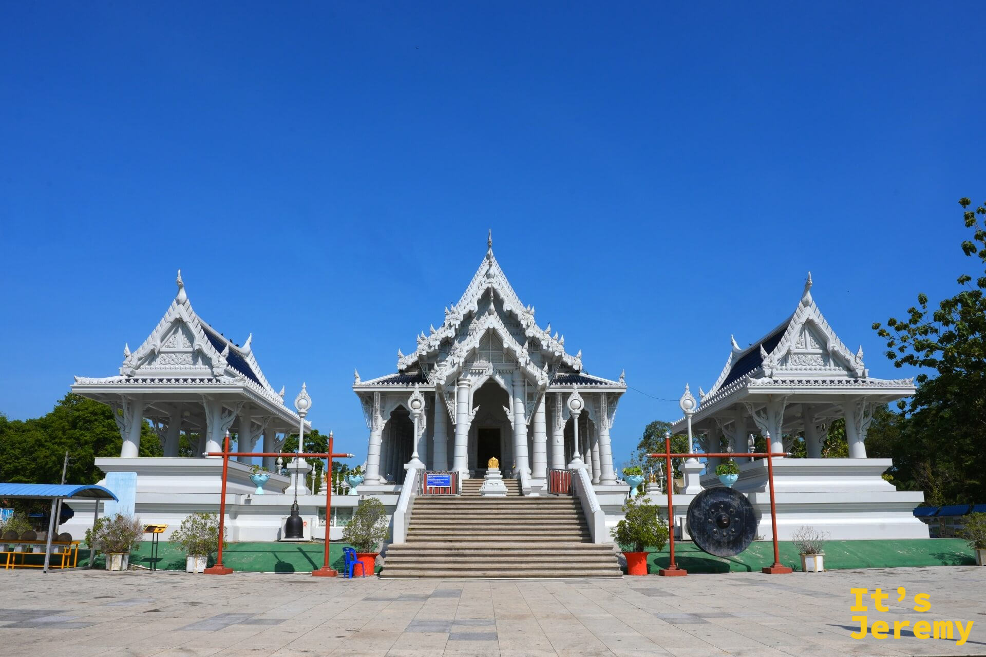 Wat Kaew Korawaram 主殿全景,三棟白殿對稱並排,前方立有銅鐘與橘紅色鐘架