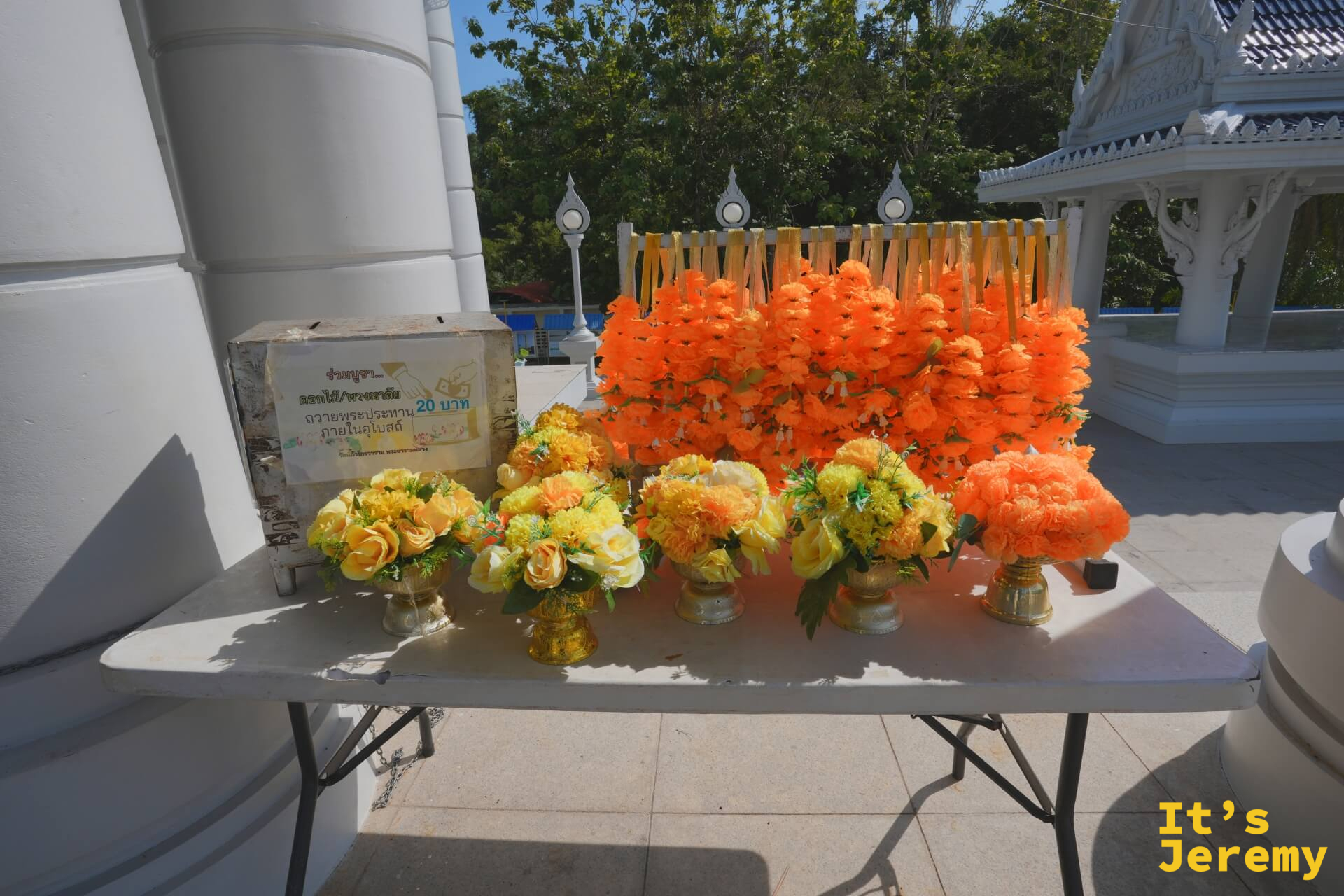 大殿廊柱旁的花環供品桌,橘色萬壽菊花環與黃色玫瑰供花,20 泰銖一串