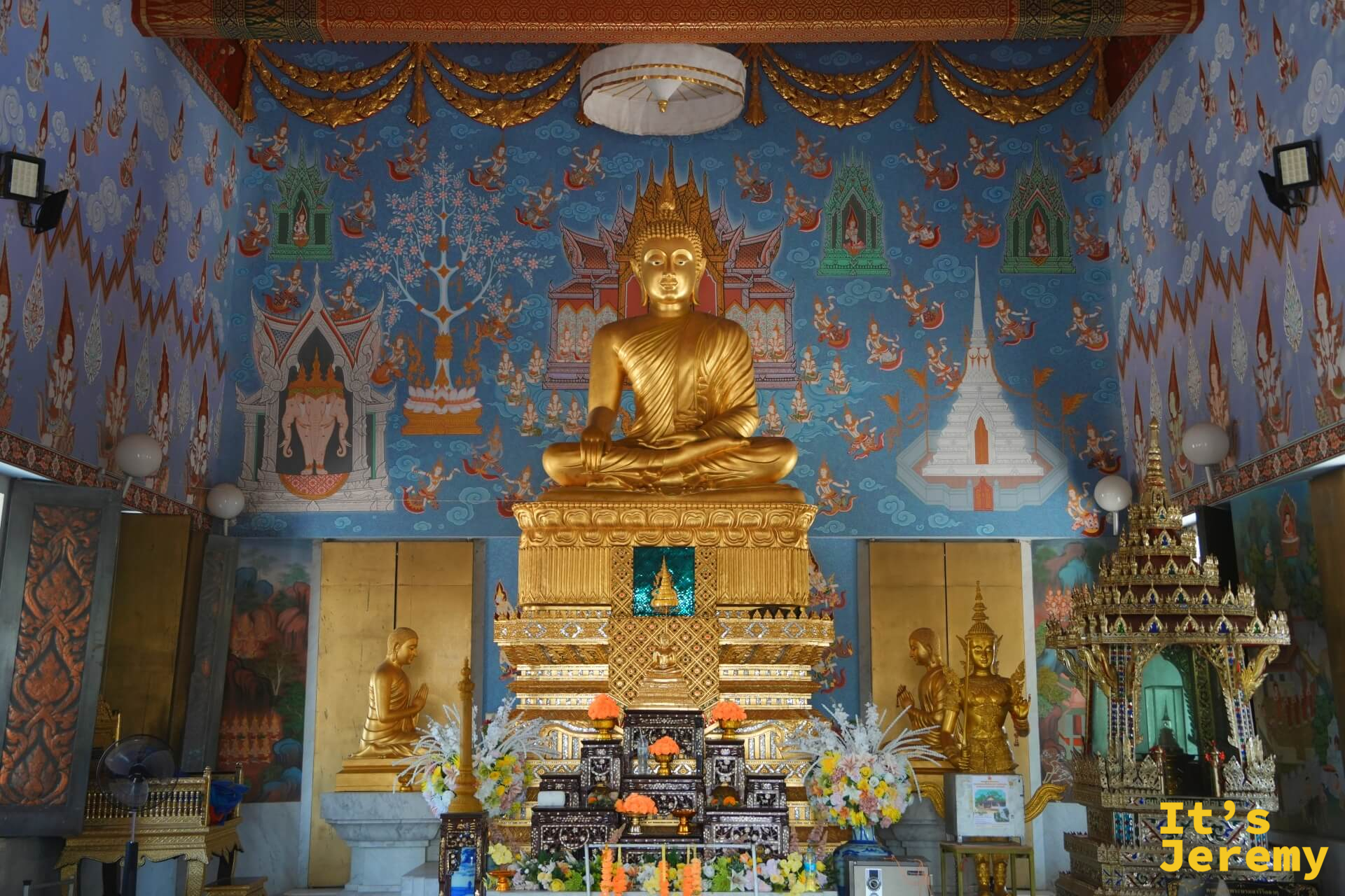 主殿全景,金色主佛與藍底壁畫,佛台兩側可見立像,花束鮮花供奉其前