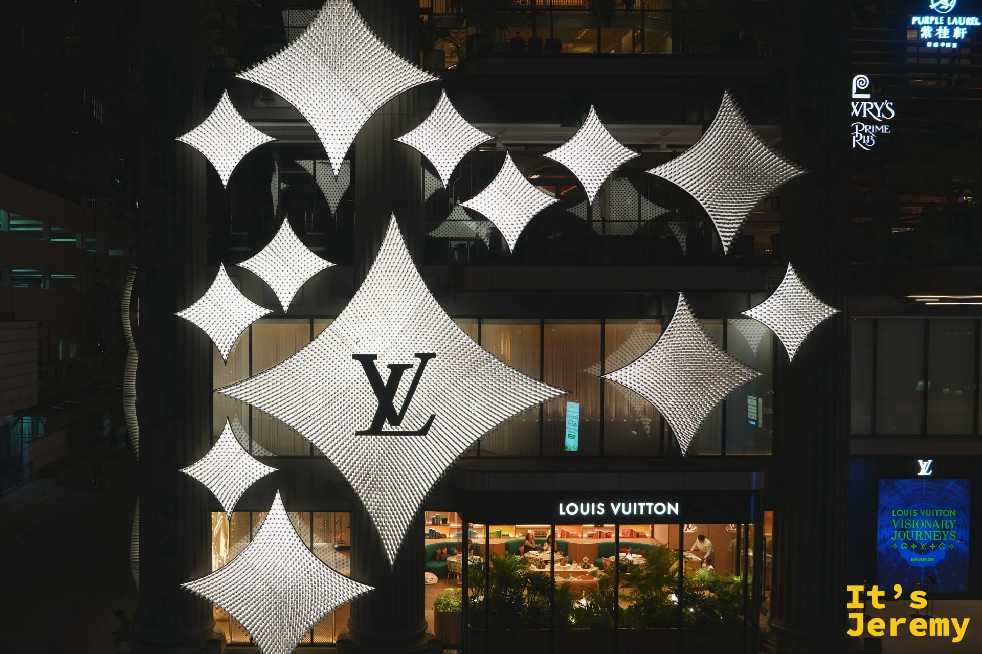 LV The Place Bangkok 外觀夜景，monogram 星形燈飾打亮整棟立面，右側可見 Visionary Journeys 招牌