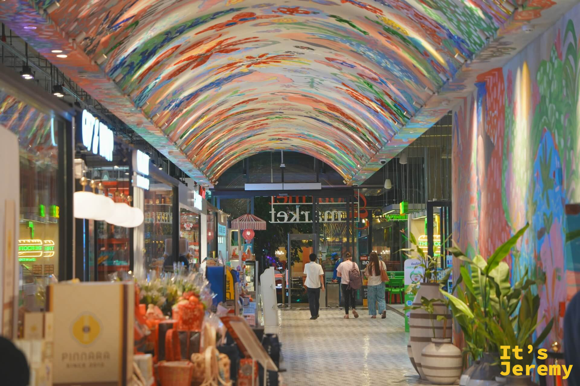 彩虹拱頂走廊,天花板滿布彩色壁畫,兩側是小店,遠處透入自然光
