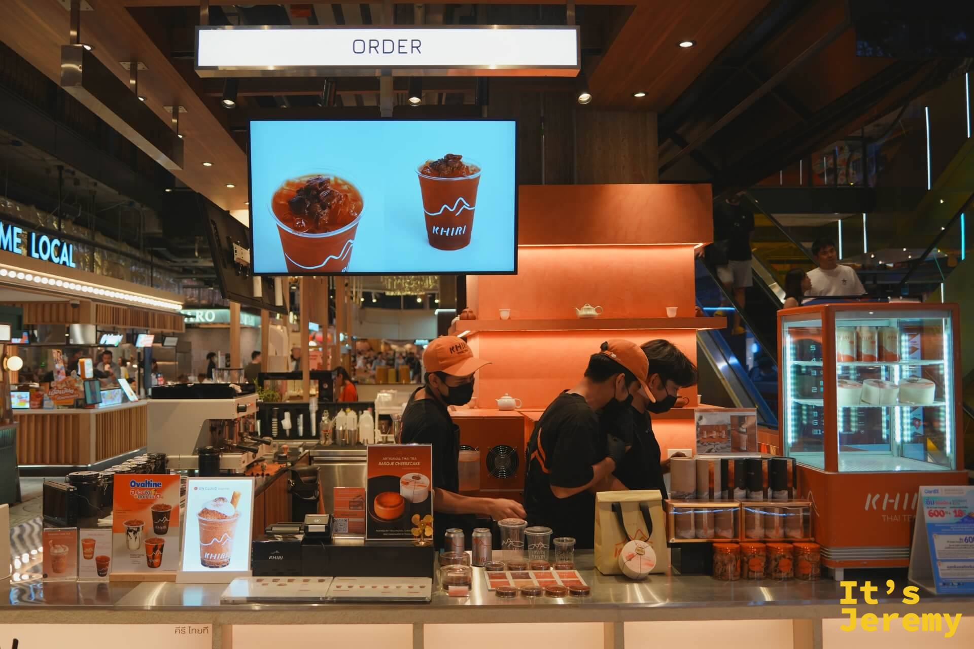 點餐台全景，橘色背牆配上展示螢幕，員工統一黑橘制服