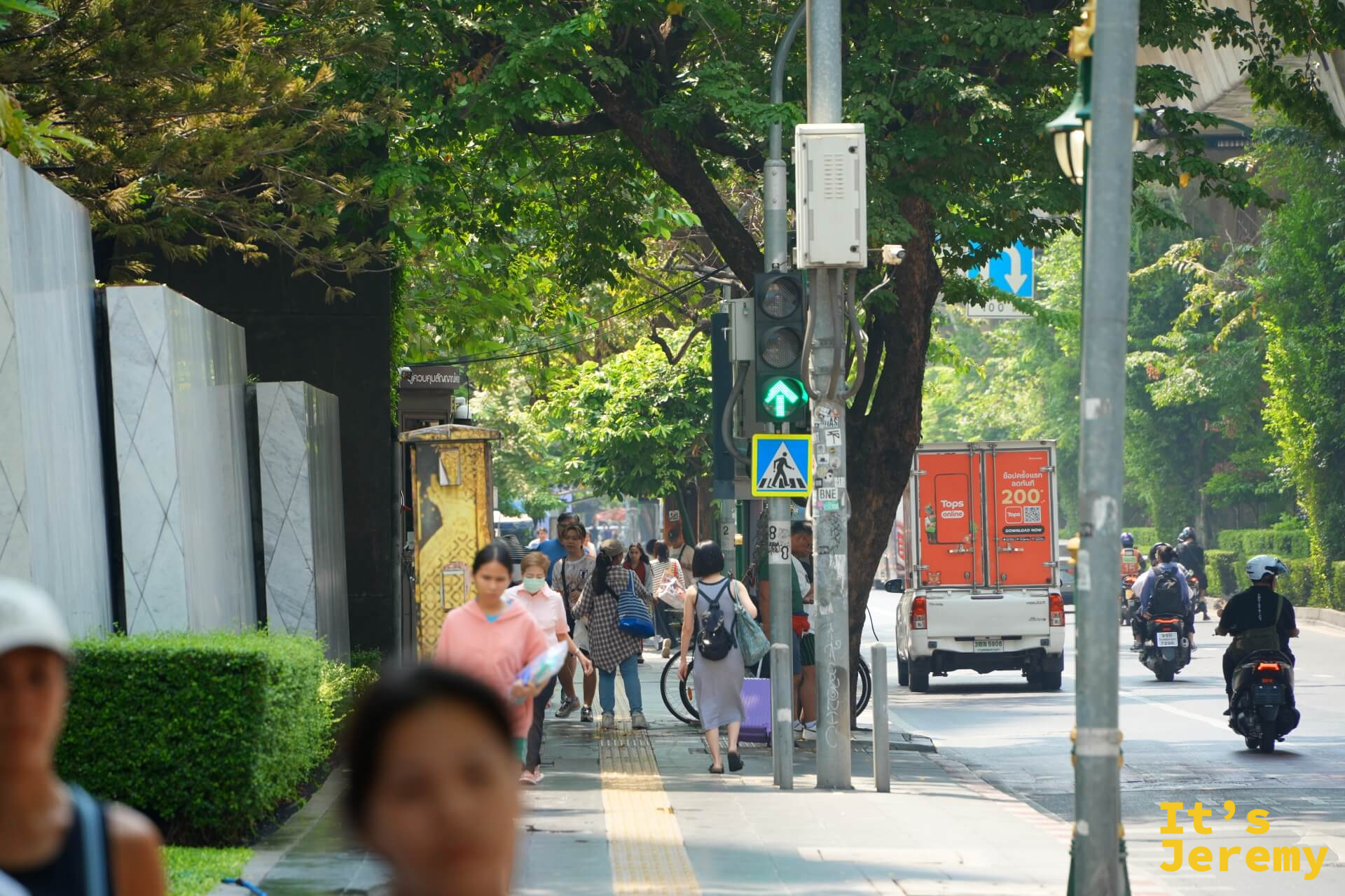 早上的蘇坤蔚路面,行人在有樹蔭的騎樓下走動,遠處是對向車流