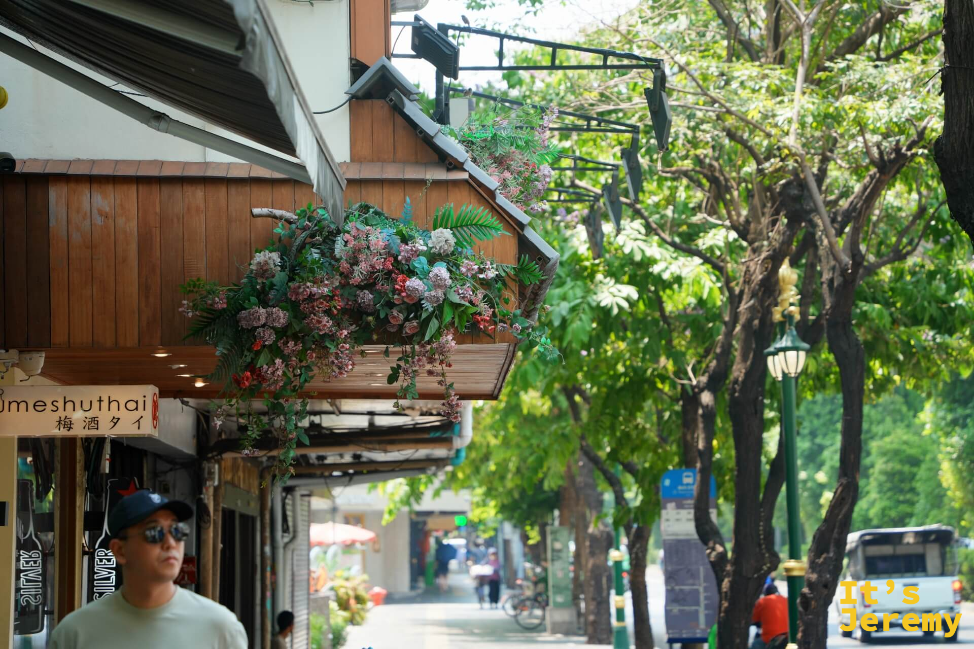 蘇坤蔚路旁商店騎樓,門口插著花的商家,路人走過,燈光和陰影在地板上切成一塊一塊