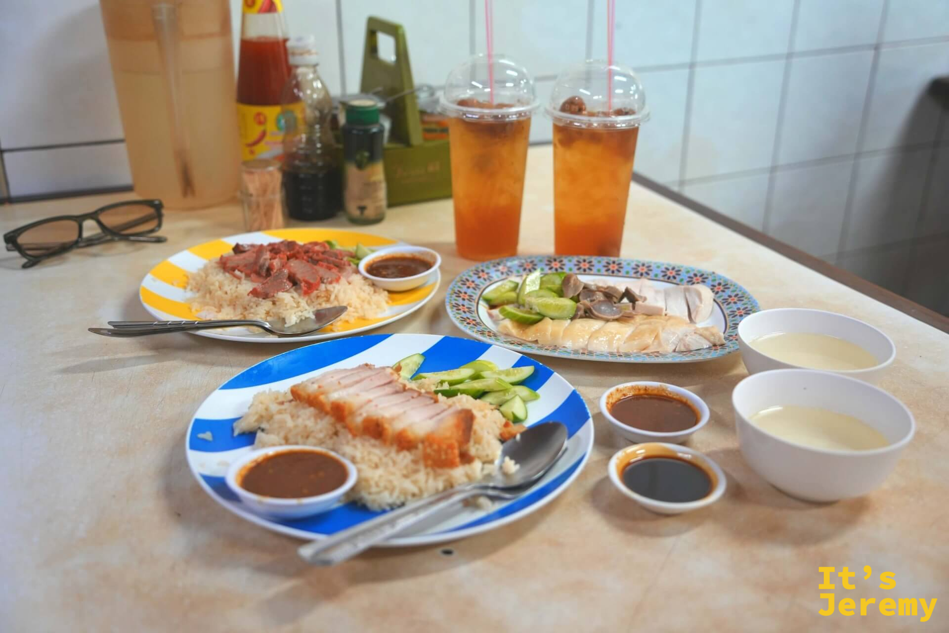 三款配飯正面視角:脆皮豬在前,紅燒肉與白斬雞在後,各附小黃瓜與醬汁,兩杯冰飲並排