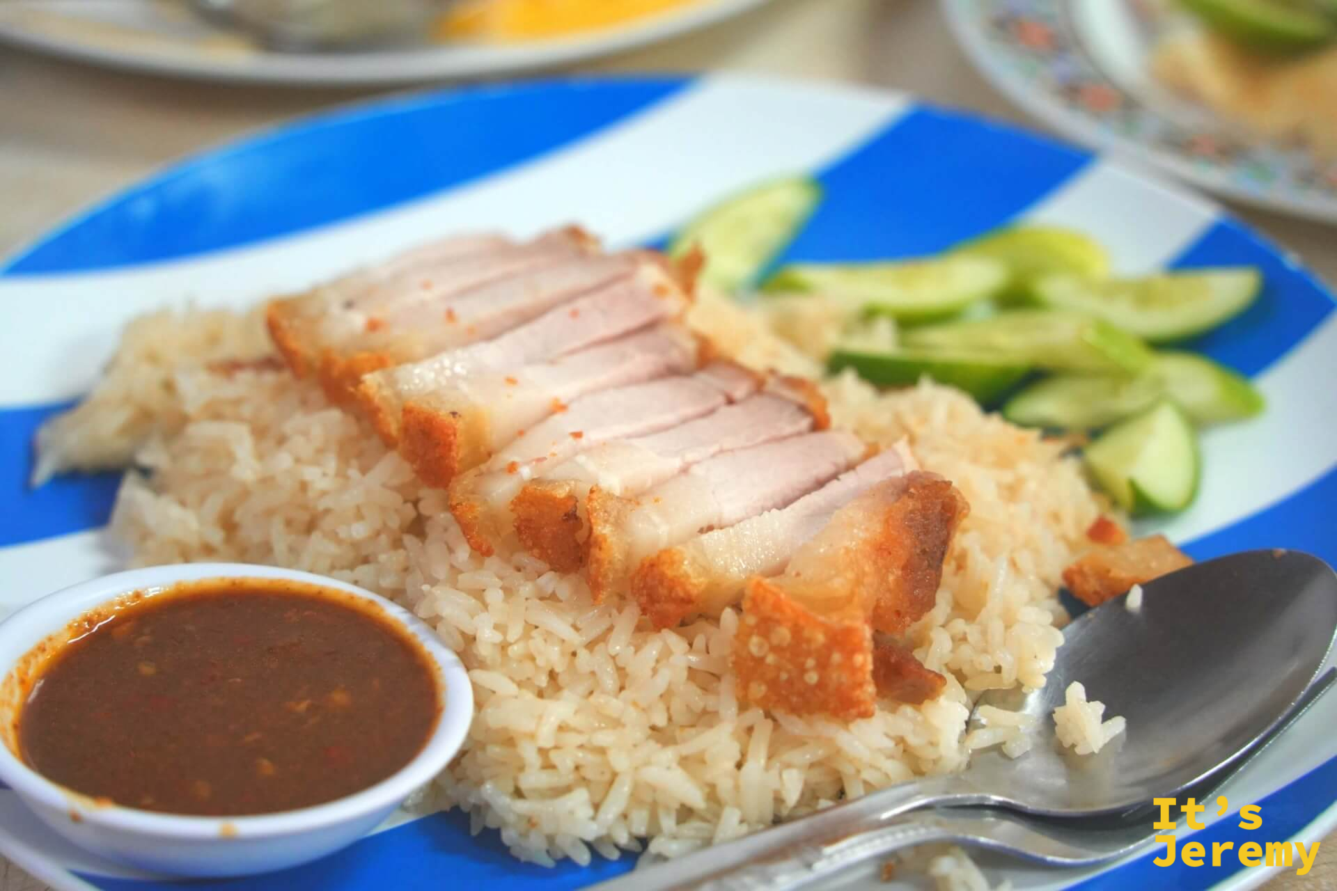 脆皮豬飯特寫,切成厚塊的脆皮豬放在白飯上,旁邊是薑蓉和辣醬,顏色對比鮮明