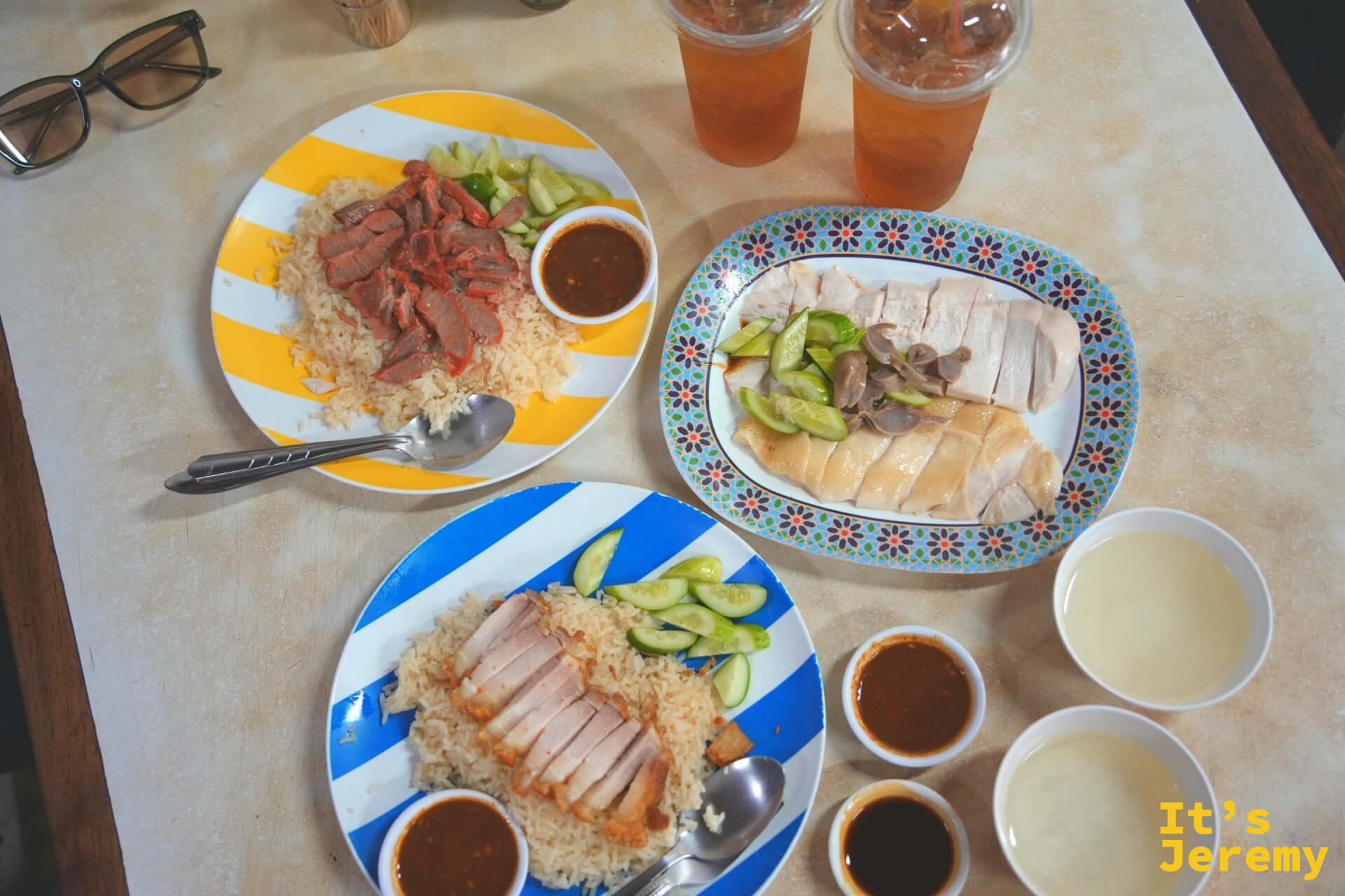 三款配飯全桌:白斬雞、脆皮豬、紅燒肉,各附醬汁與小黃瓜,加上兩杯冰飲,俯瞰全景