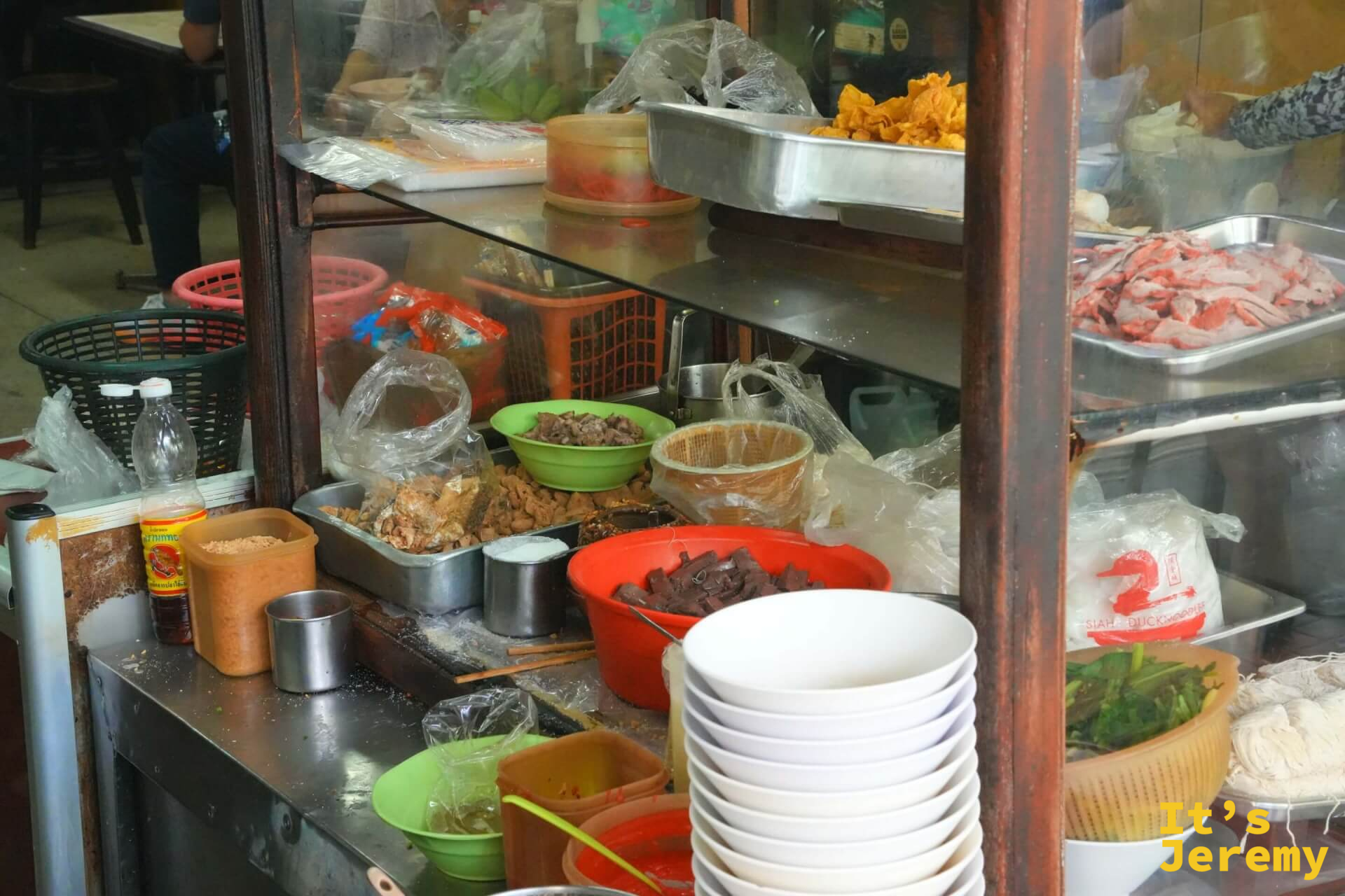 廚房備料台:玻璃櫃中分置各色肉類食材與配料,白色湯碗整齊疊放待用