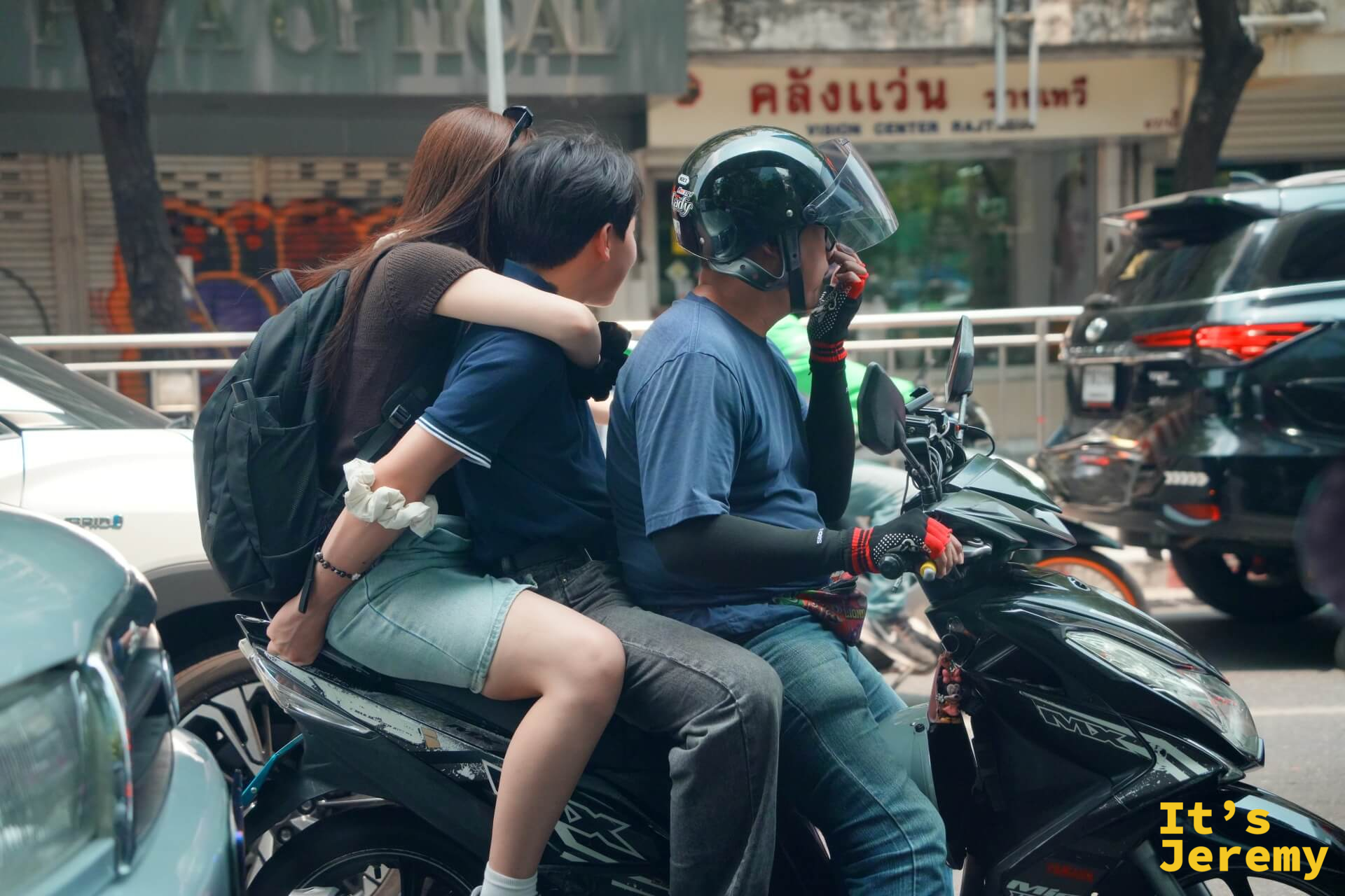 一對情侶搭摩托計程車,女生側坐在後座,摩托車司機悠閒地滑著手機等綠燈