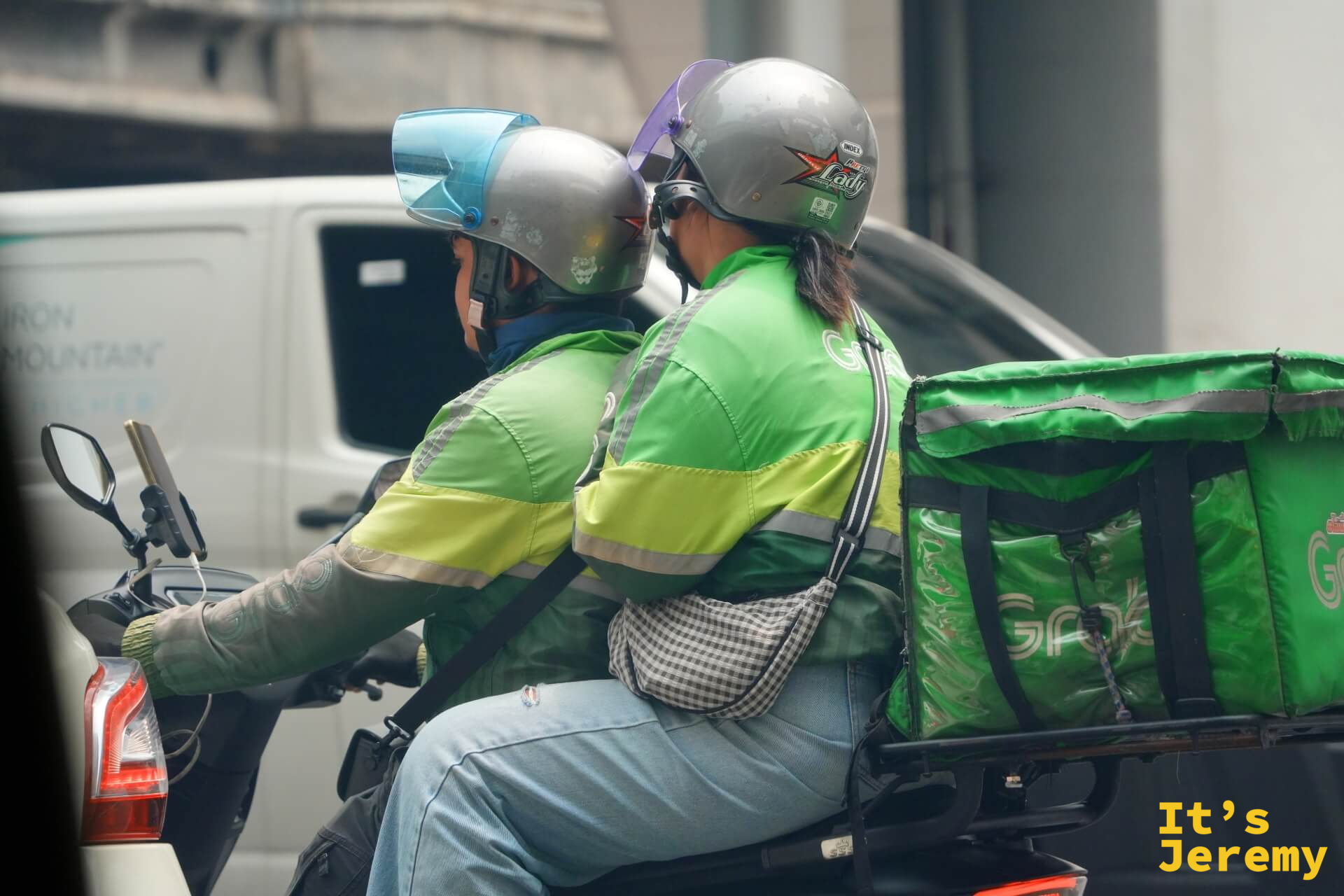 兩位 Grab 外送員共乘一輛機車,後座的人揹著外送保溫箱,像是正要出任務的搭檔