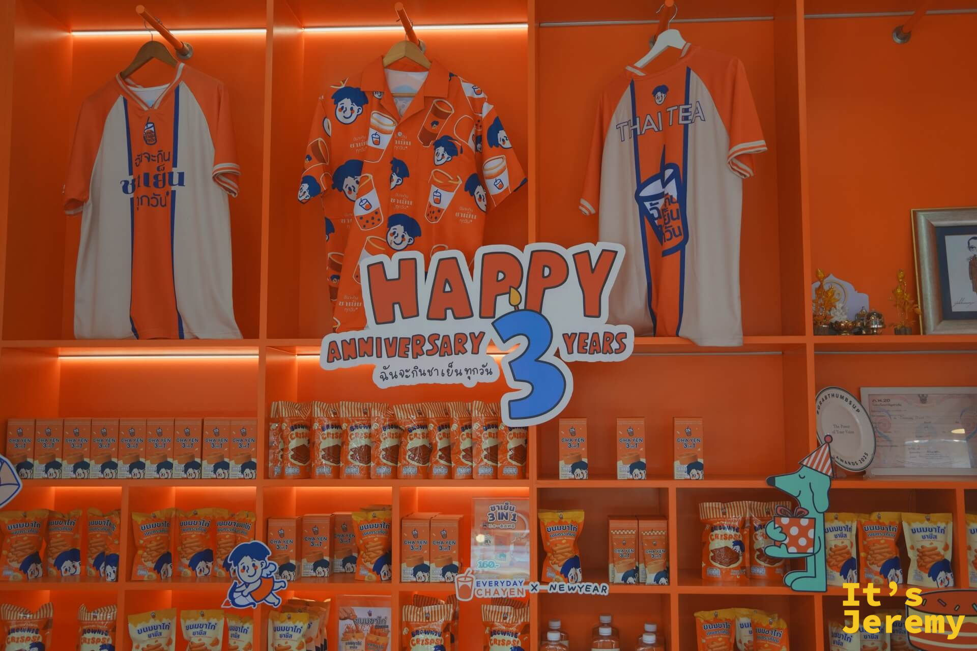 品牌展示架:Thai Tea 印花 polo 衫與運動衫,下方擺滿聯名零食包,Happy 3 Years Anniversary 立體字居中