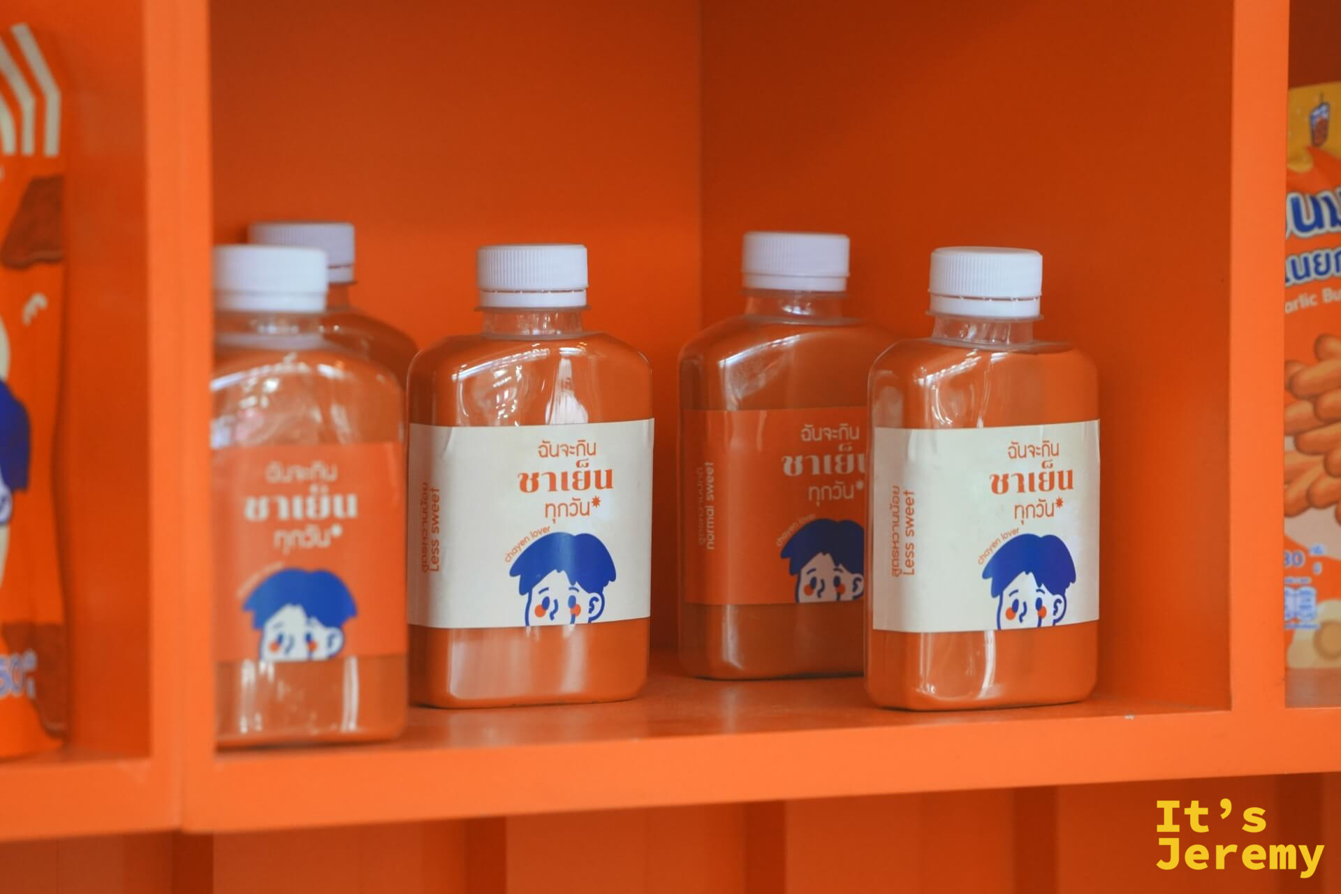 展示架上的瓶裝泰式冰茶,標示 Less Sweet 與 Normal Sweet,背景是橘色展示格