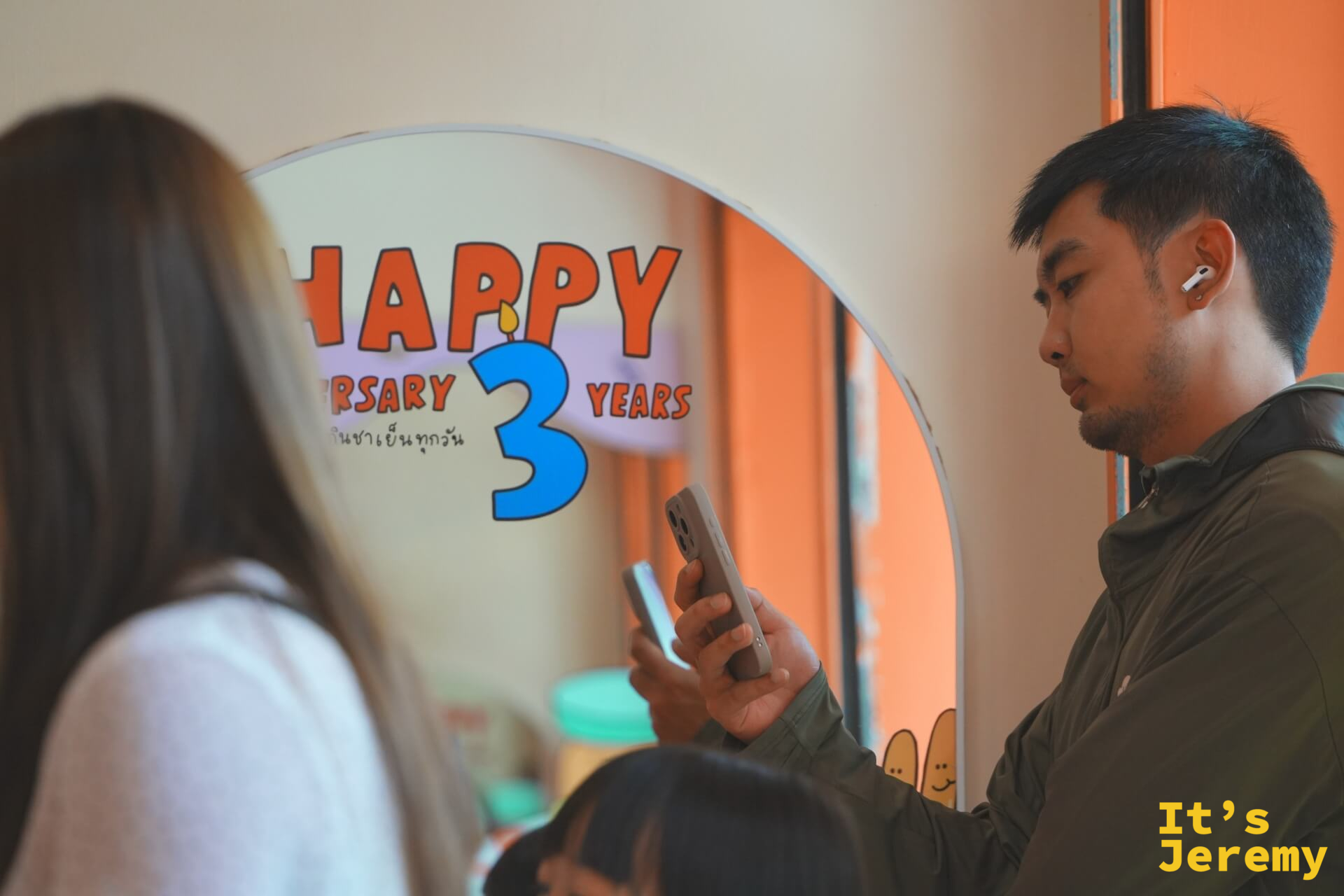 顧客手持手機在 Happy Anniversary 3 Years 拱形鏡前拍照,前景為另一位顧客的背影