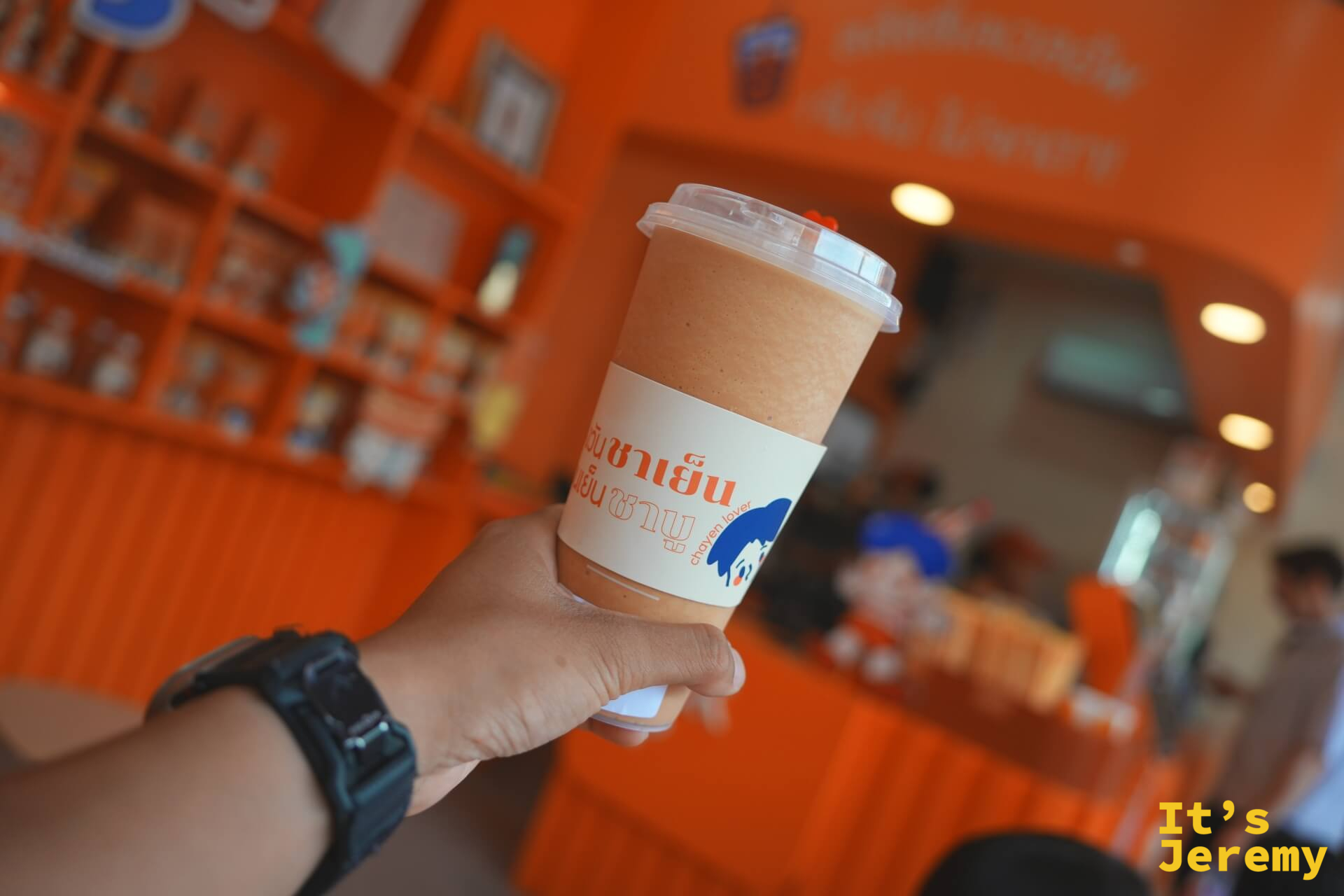 手持 Everyday Thai Tea 品牌杯,橘色杯身在陽光下顯色飽和,BTS 站出口的陽光從背後打進來