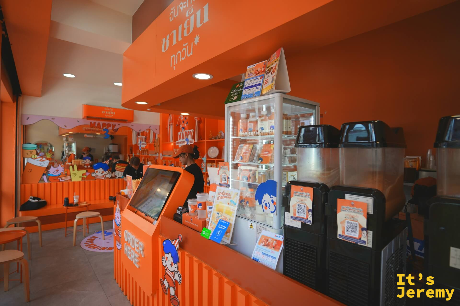店內點餐機台與冷藏展示冰箱,右側為製茶區,整體採全橘色設計