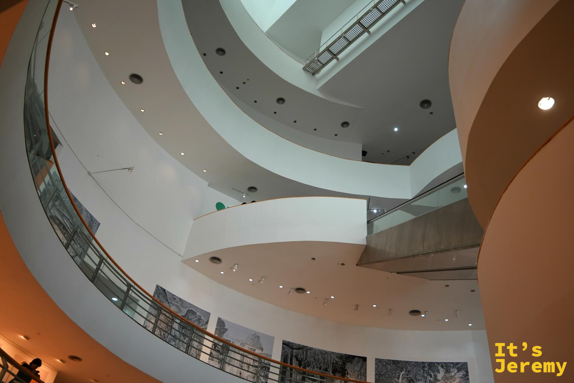 從螺旋走廊仰視較低樓層，黑白水墨風格大型展覽作品沿牆鋪展，訪客在光影間行走