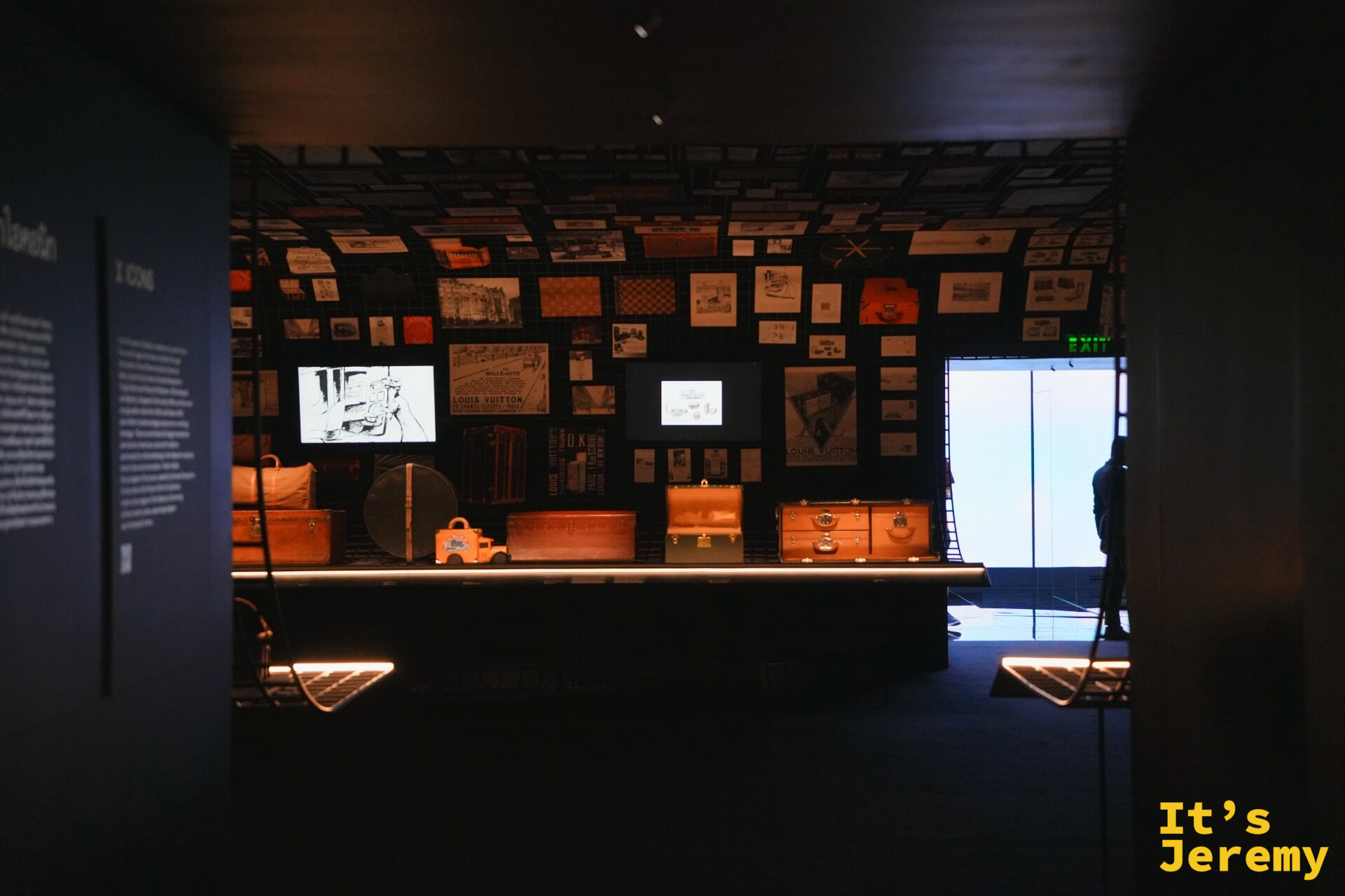 Origins 歷史檔案室全景，展台上排列多款不同年代行李箱，背景大螢幕與滿牆老廣告形成強烈縱深