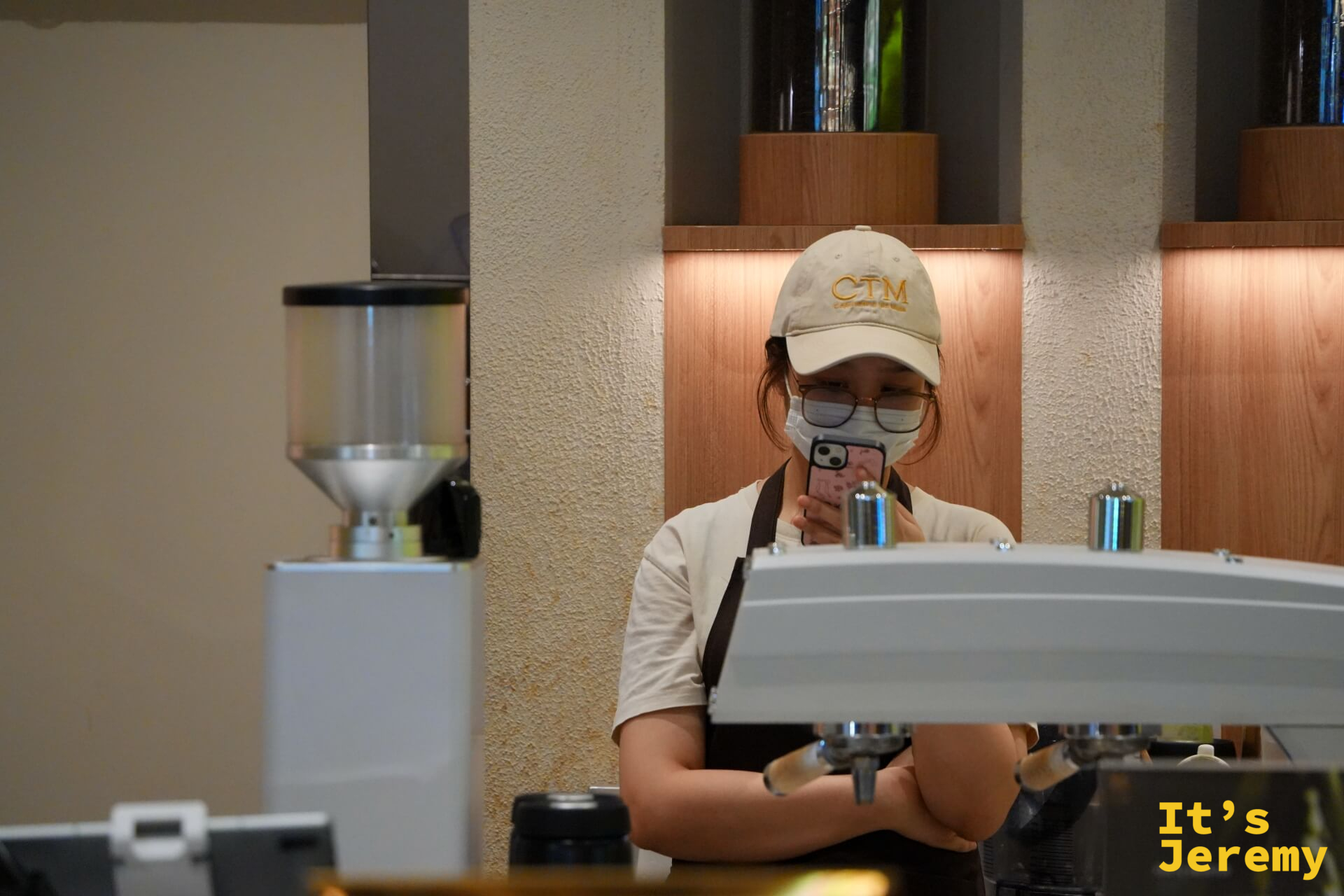 女性店員空檔低頭滑手機,espresso 機與磨豆機在旁待命