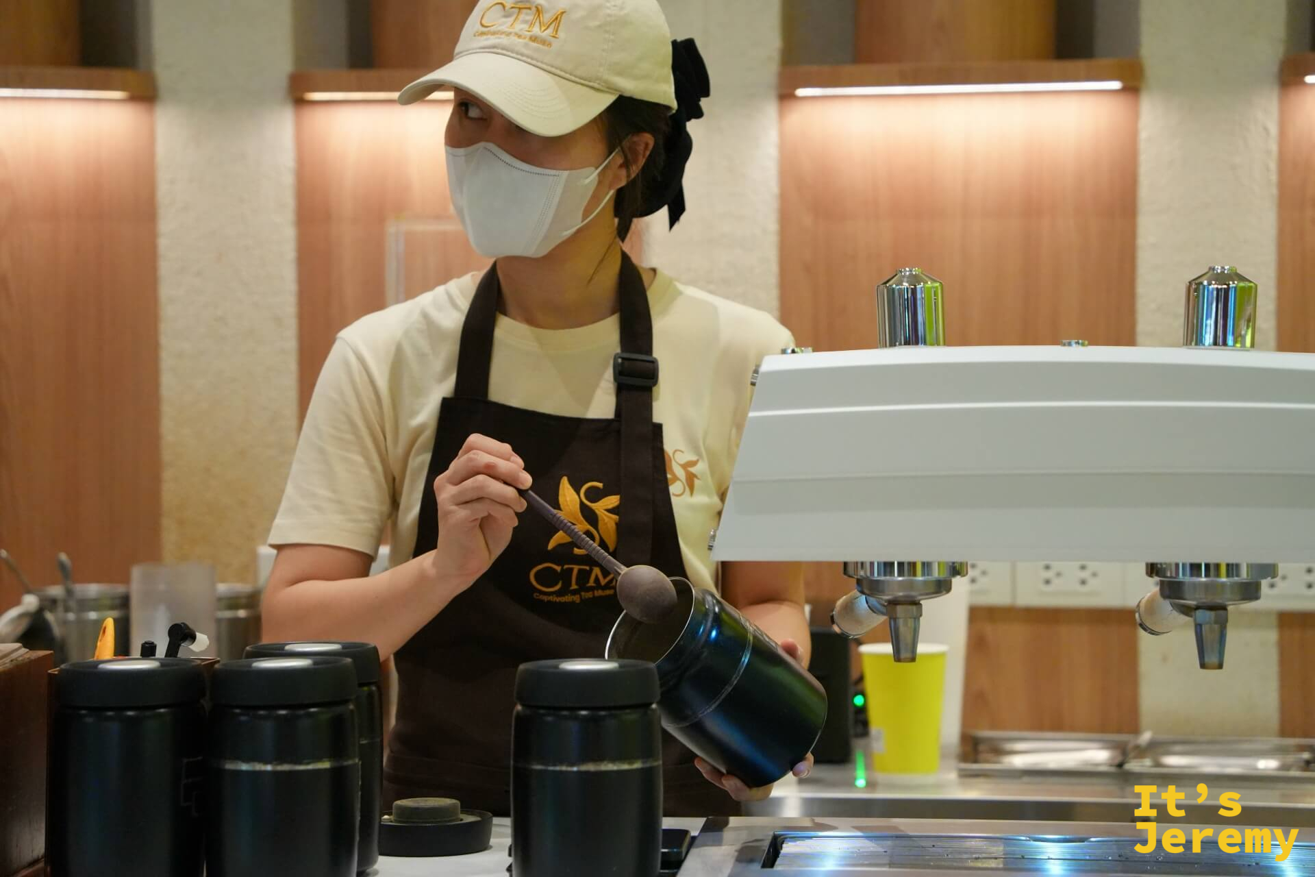 女性店員攪拌拿鐵,深色圍裙上繡有 CTM 花葉 logo