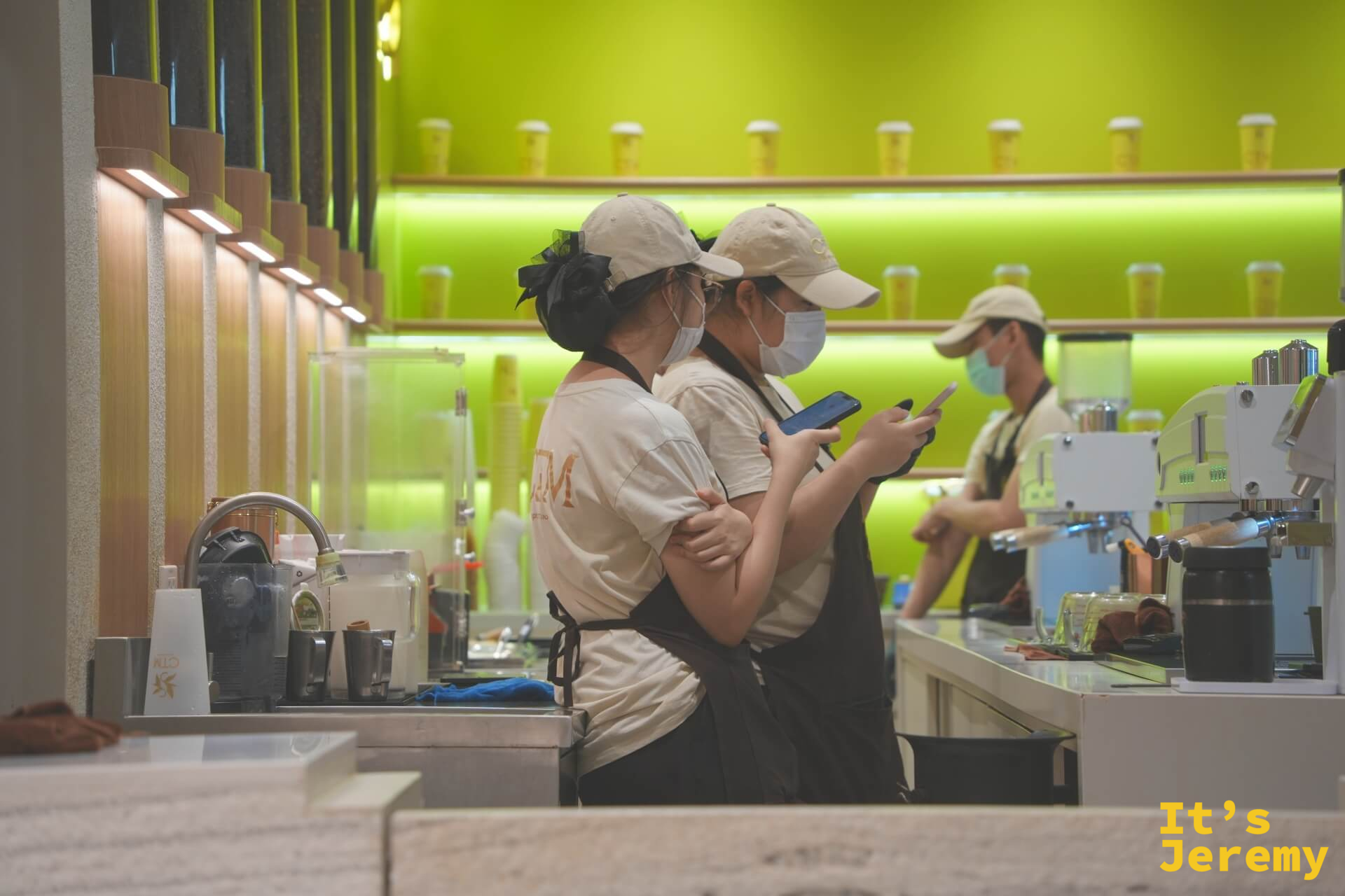 兩位女性店員並排滑手機,右側另一位正在備料