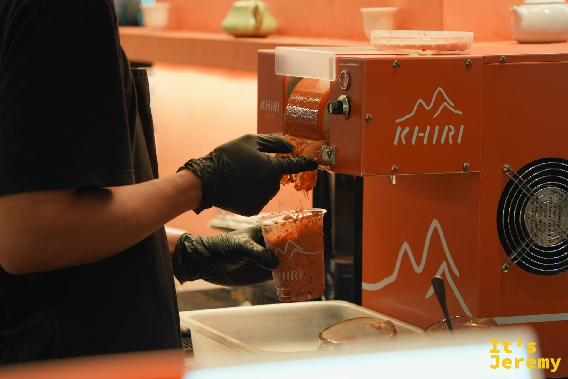 KHIRI Thai Tea 的品牌刨冰機,全橘色外殼,師傅正在用機器將泰茶冰磚刨成細雪泥狀,現場備料是這個攤位最吸引目光的視覺