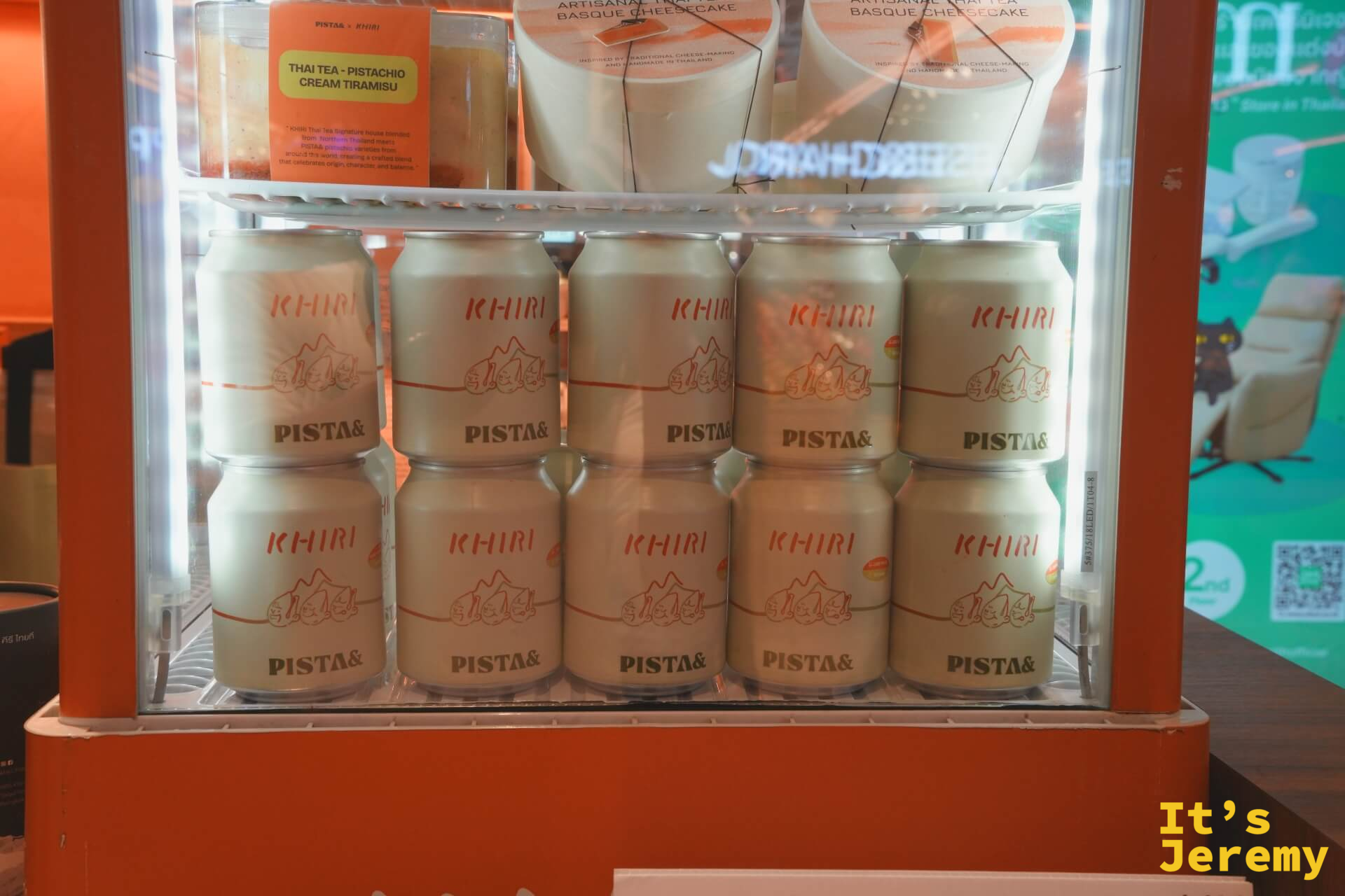 展示冰箱另一層：KHIRI × PISTA& 聯名罐裝佔滿整排，上層放著 Basque Cheesecake 和 Tiramisu 聯名甜點