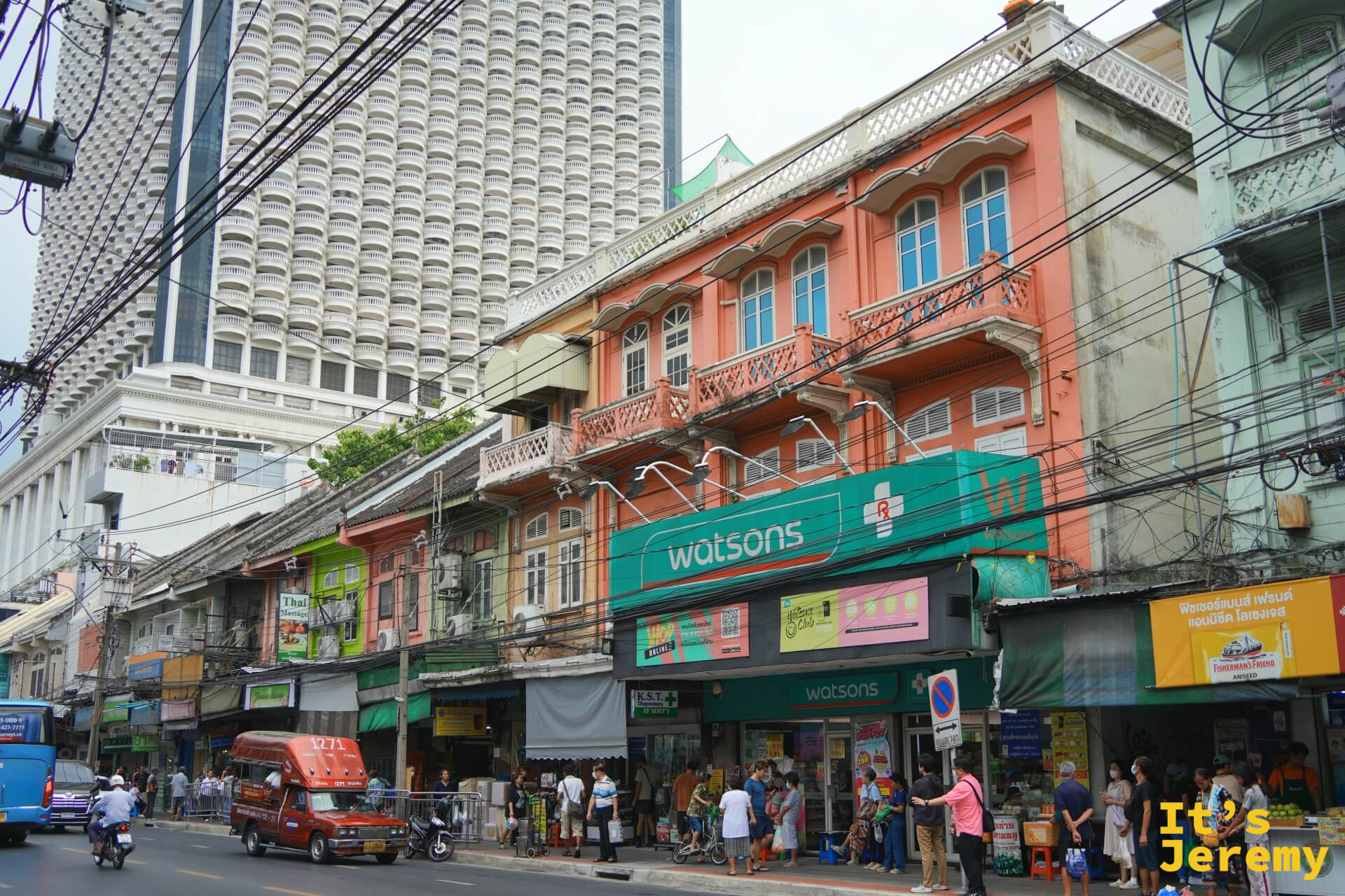 粉紅色兩層老店屋的 Watsons,背後是現代蜂巢格玻璃帷幕高樓,前景紅色嘟嘟車