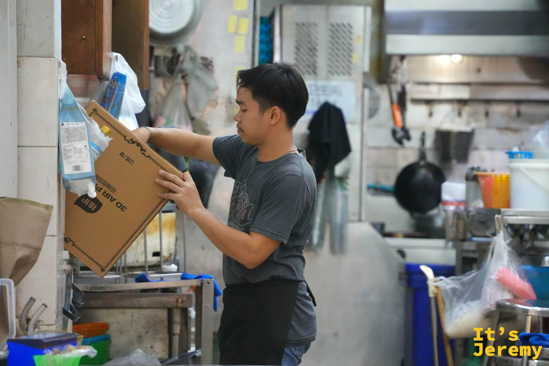 後廚工作人員在廚房搬運紙箱,周圍是各式廚具和儲物架