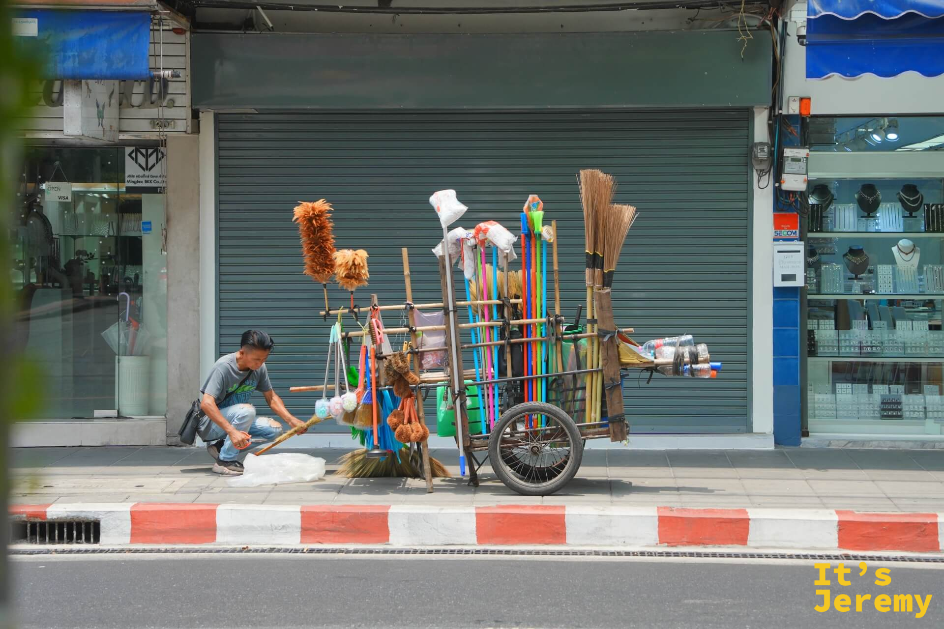 路邊流動攤販推著滿車彩色掃把和清潔用具,停在半拉的鐵捲門前